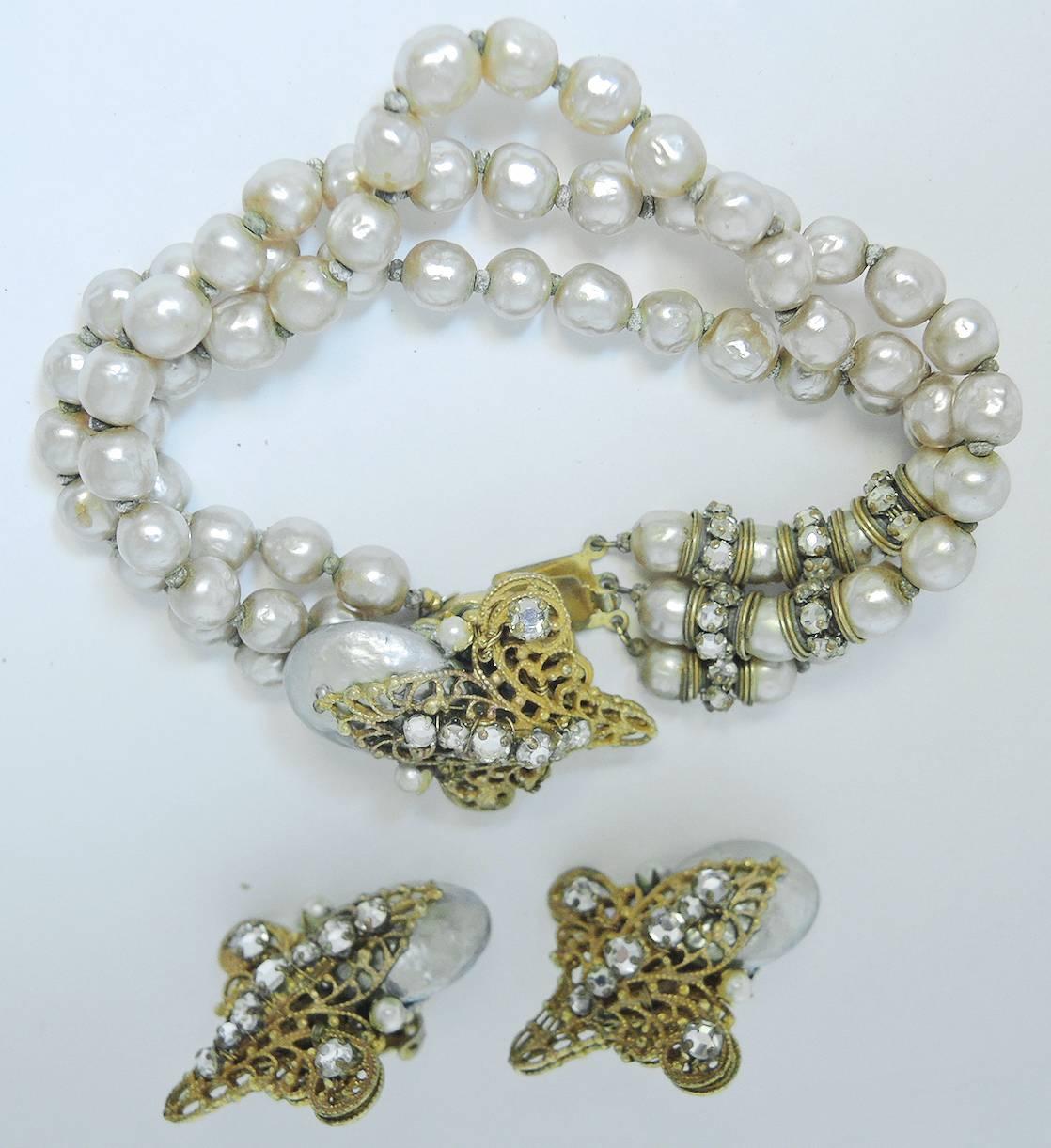 This bracelet has 3 strands of faux pearls. It has rondell spacers in the front on one side. The centerpiece has a large baroque pearl with rose montee stones.  It is in a gold tone open work setting. The bracelet measures 7-1/2” x 3/8”. The