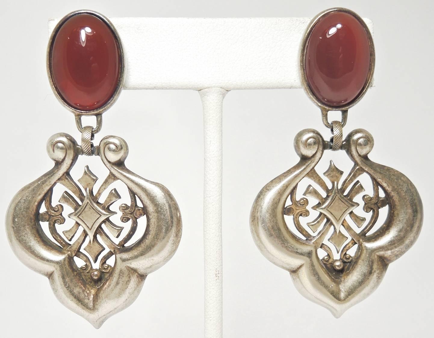 These earrings were made with a faux carnelian cabochons on top. The bottom has a scallop and open work design in a brass tone setting, it measures 2-1/2” x 1-1/4”. It is in excellent condition.