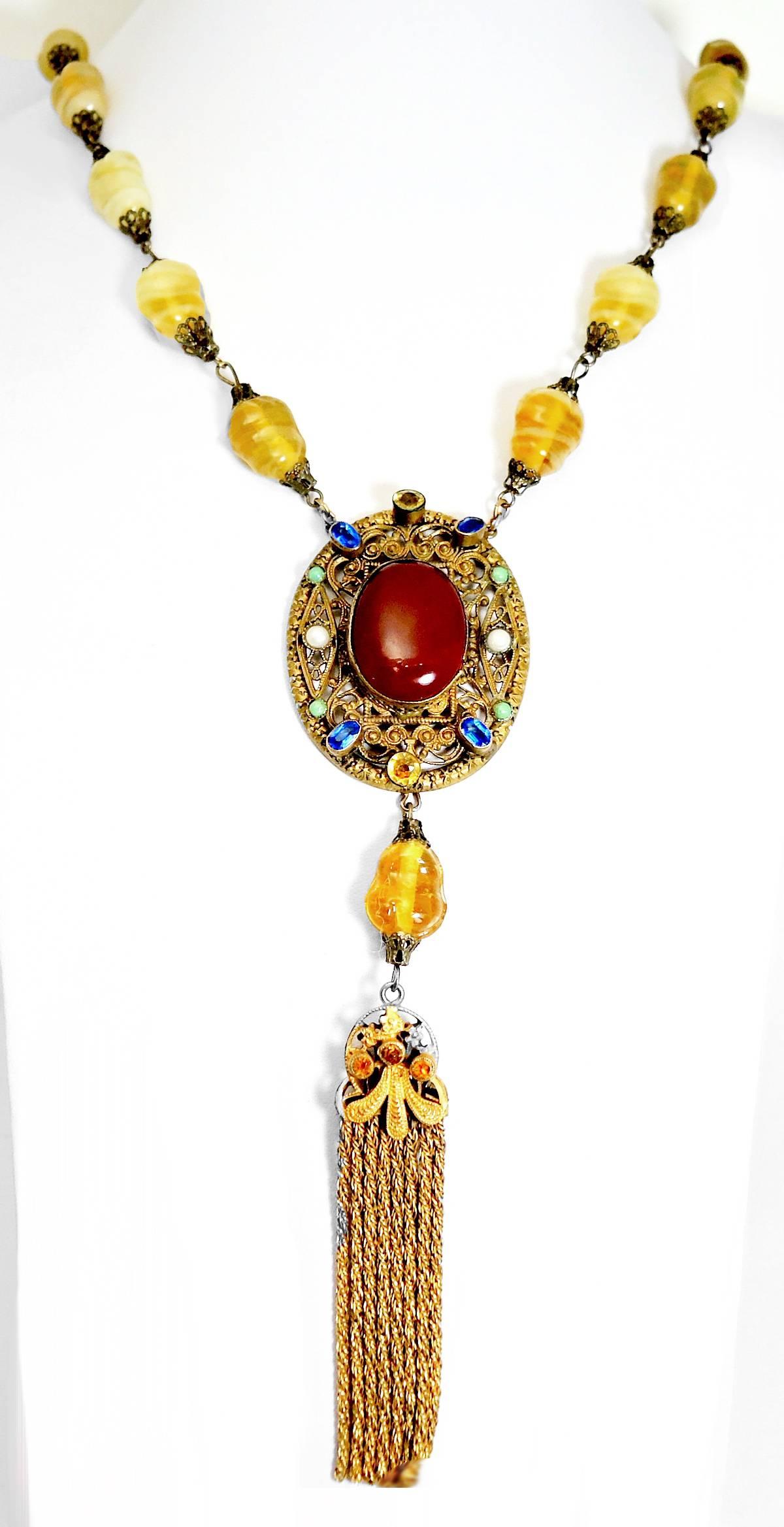 This 1930’s Czech necklace is made with yellow poured glass. Each piece is spaced with brass connectors. It leads to a beautiful centerpiece that has a round faux carnelian stone in the center. The pendant also has blue, green and white glass