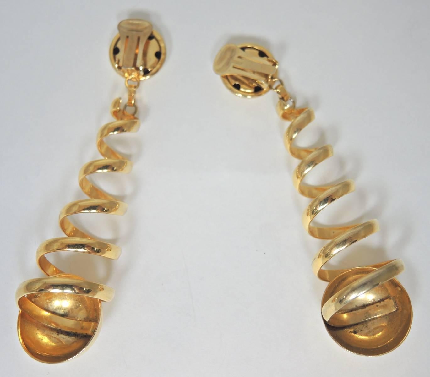 These earrings make a great conversation piece. The top is a button earring that connects to a long coiled dangling design. It ends with another larger button at the bottom. It is in a gold tone setting and measures 4” x 1”.  It is in excellent