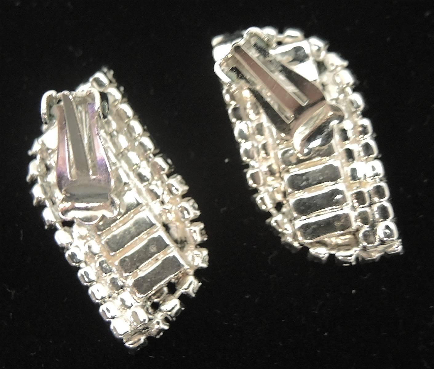 These vintage clip earrings have a row of baguette rhinestones in the center with round rhinestones at the border. They have a leaf design and measure 1-1/2” x 3/8”. They are in a silver tone setting and are in excellent condition. 