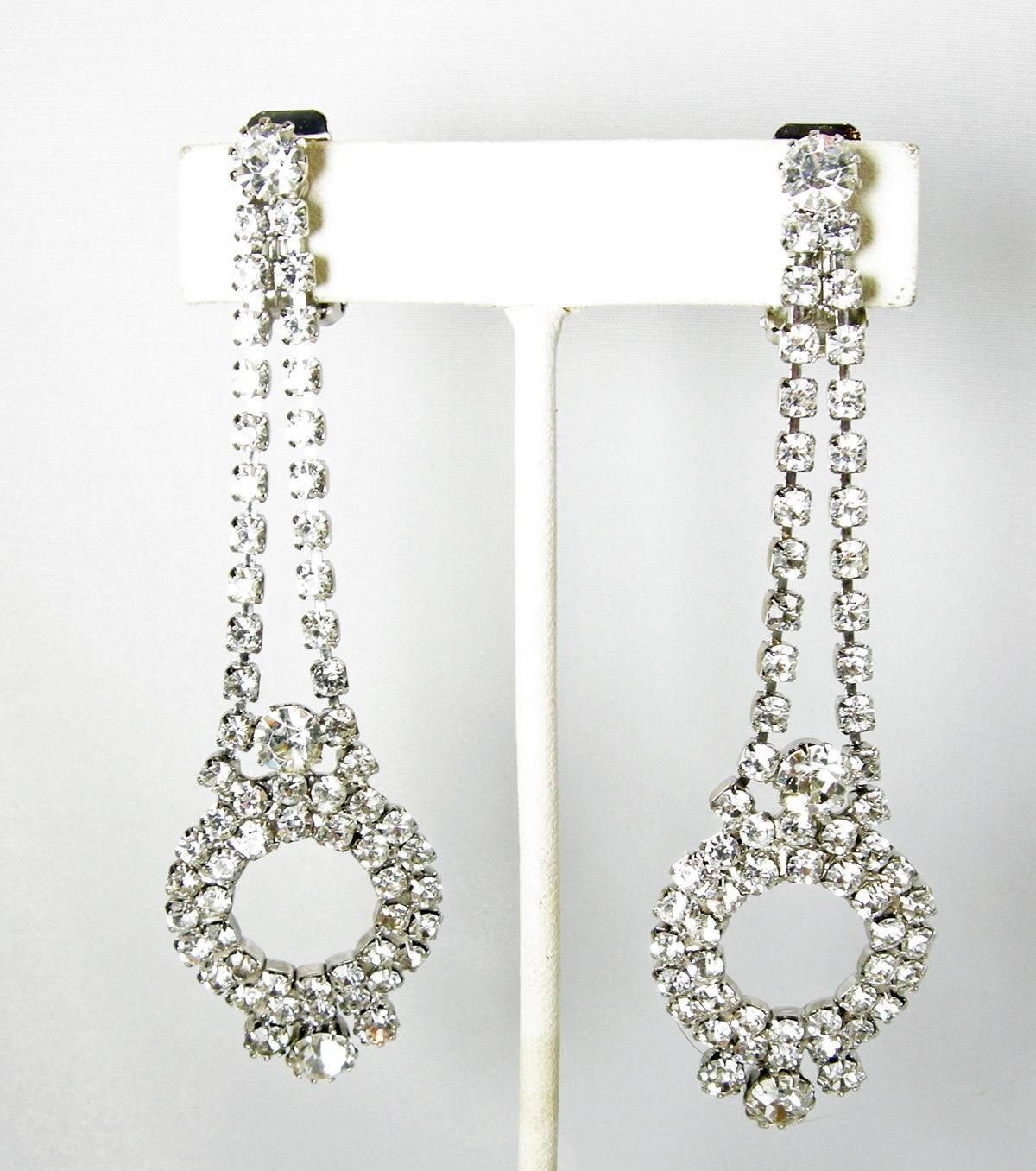 These earrings have a Deco style and are made with beautiful clear rhinestones that lead to a bottom circular opening. There are 3 round rhinestones at the base. These clip earrings are set in a silver tone setting and measure 3-1/2” x 1”. They are