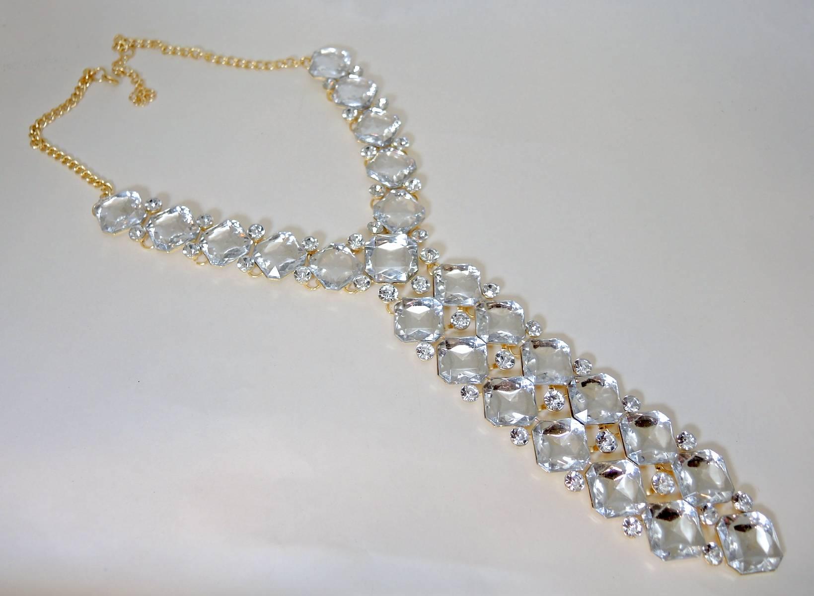 This is a glitzy, fashionable waterfall necklace that has abundance of large rectangular and smaller clear resin like crystals. It is made in a gold tone setting and measures 23” x 1/4”. The centerpiece measures 8” x 2”. It has a lobster clasp and