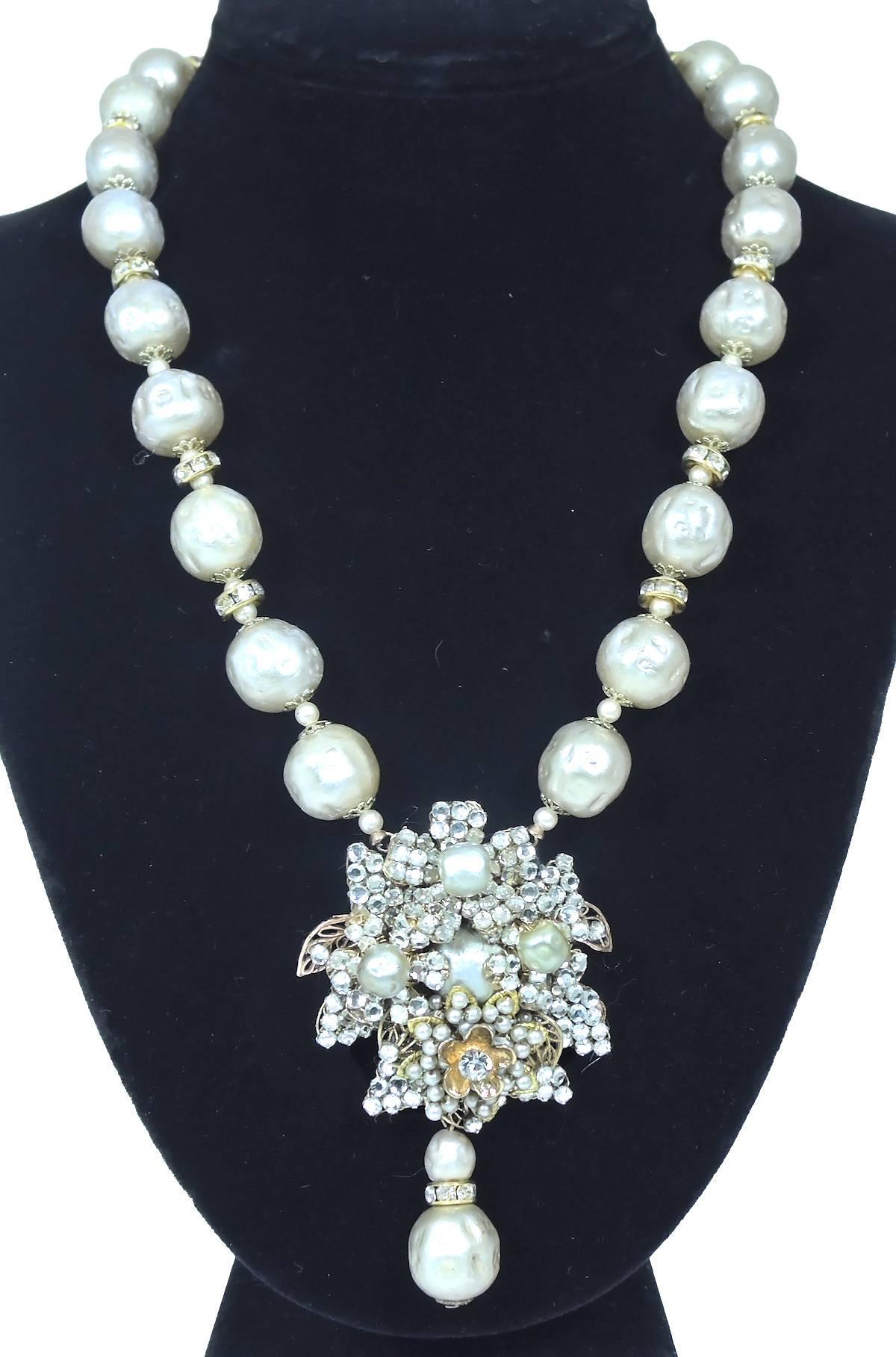 This is a vintage 1950s Miriam Haskell Necklace is made with large faux baroque pearls and rondell spacers. The necklace leads down to a gorgeous floral centerpiece that is embellished with rose montee stones. It has a large faux pearl in the center
