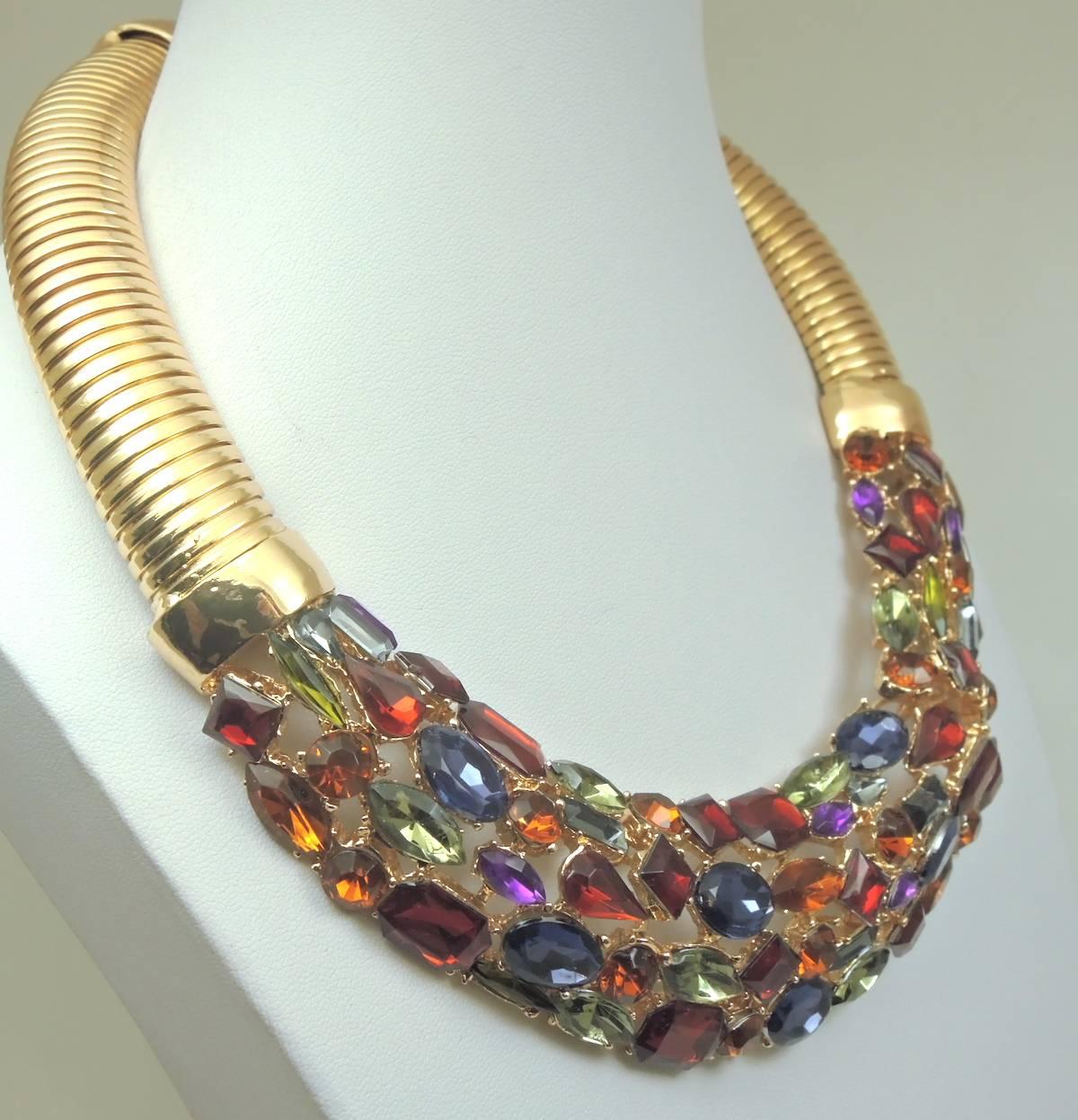 This wonderful wide collar necklace was designed with prong set multi sized and colorful glass stones. It was made with a flexible ribbed chain and measures 19” x 1-1/2” at the widest part. It has a lobster clasp and is in a glossy gold tone