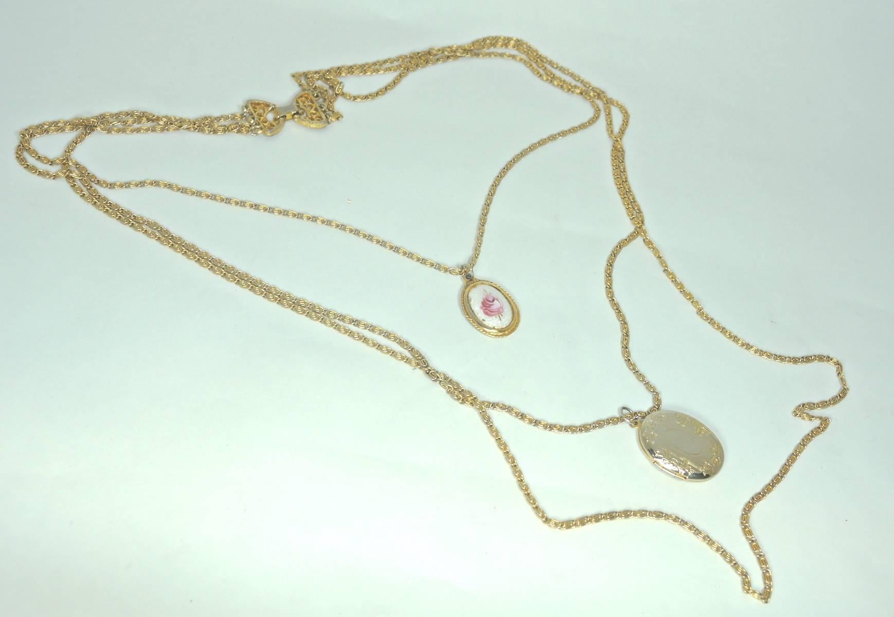 This Goldette necklace features three chains with the longest measuring 34”. The second to longest has a locket and measures 26”. The shortest chain has a small single pink rose enamel pendant that measures 20”. This necklace was designed in a gold