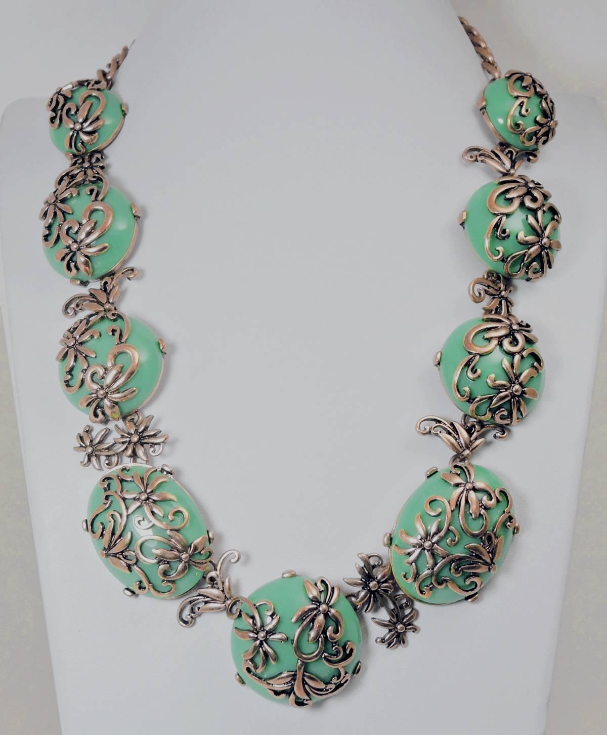 This is a statement necklace made by Oscar De La Renta featuring dome shaped faux green turquoise stones with a gold tone floral open work design over each stone. This necklace has a lobster clasp and measures 22” x 1-12”.  It is signed “Oscar De La