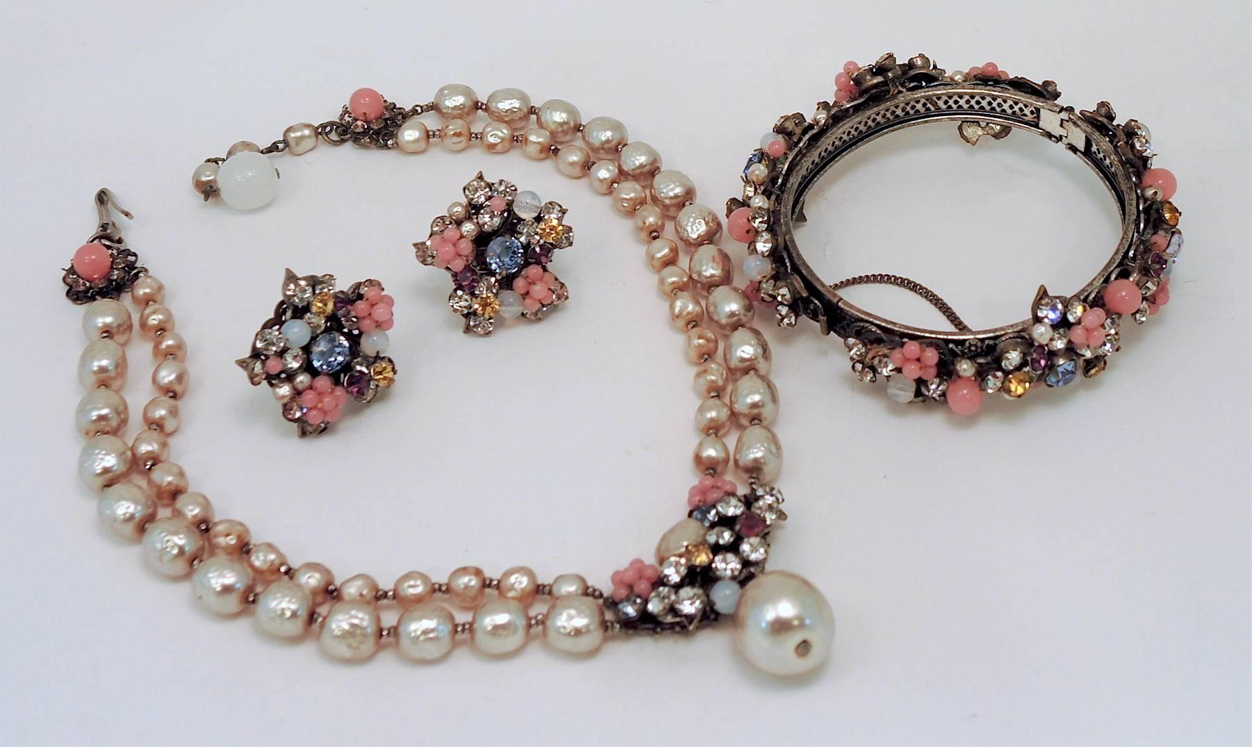 This is quite a find. This Miriam Haskell parure features a double strand necklace made of faux baroque pearls leading down an intricate centerpiece. The centerpiece has a pink glass flower on each side and rose montee stones with a large baroque