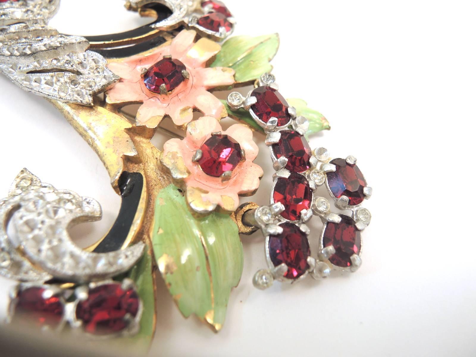 This cornucopia brooch is sprouting out pink enamel flowers centered with round red rhinestones and green enamel leaves with red rhinestone spray on top. The cornucopia is encrusted with clear rhinestone and accented with red rhinestones. It was has