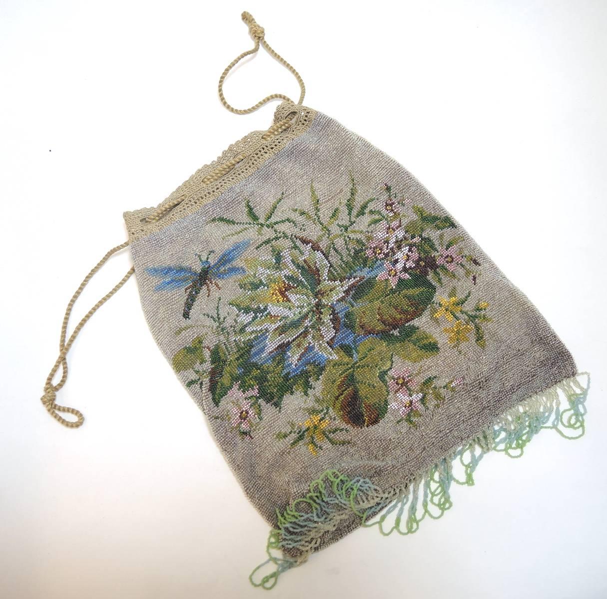 This is a lovely steel beaded purse with a botanical floral motif on a dove gray beaded background.  It has a beige croche finish to the drawstring, making it different from other purses  It measures 9” x 10” has multicolor fringe adding another 2