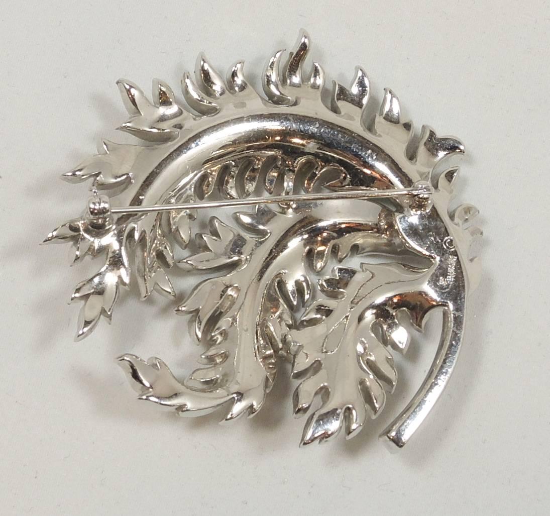 This is a lovely and well executed Trifari Plume brooch featuring delicate rhinestones and baguettes in a silver tone setting. This brooch measures 2-1/2” x 2-1/2” and signed “Trifari” with the crown over the T.  It is in excellent condition.
