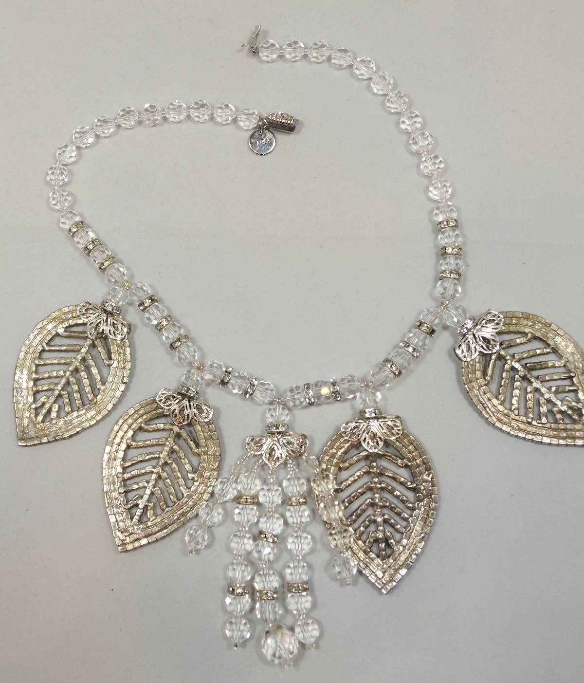 This one of a kind Anka necklace features a crystal bead necklace with four large sized crystal leaves centered with 4 dangling crystal rows. It has a slide in floral clasp. It measures 17” x 1/4” The leaves measure 2-1/2” x 1-1/2”. It is signed