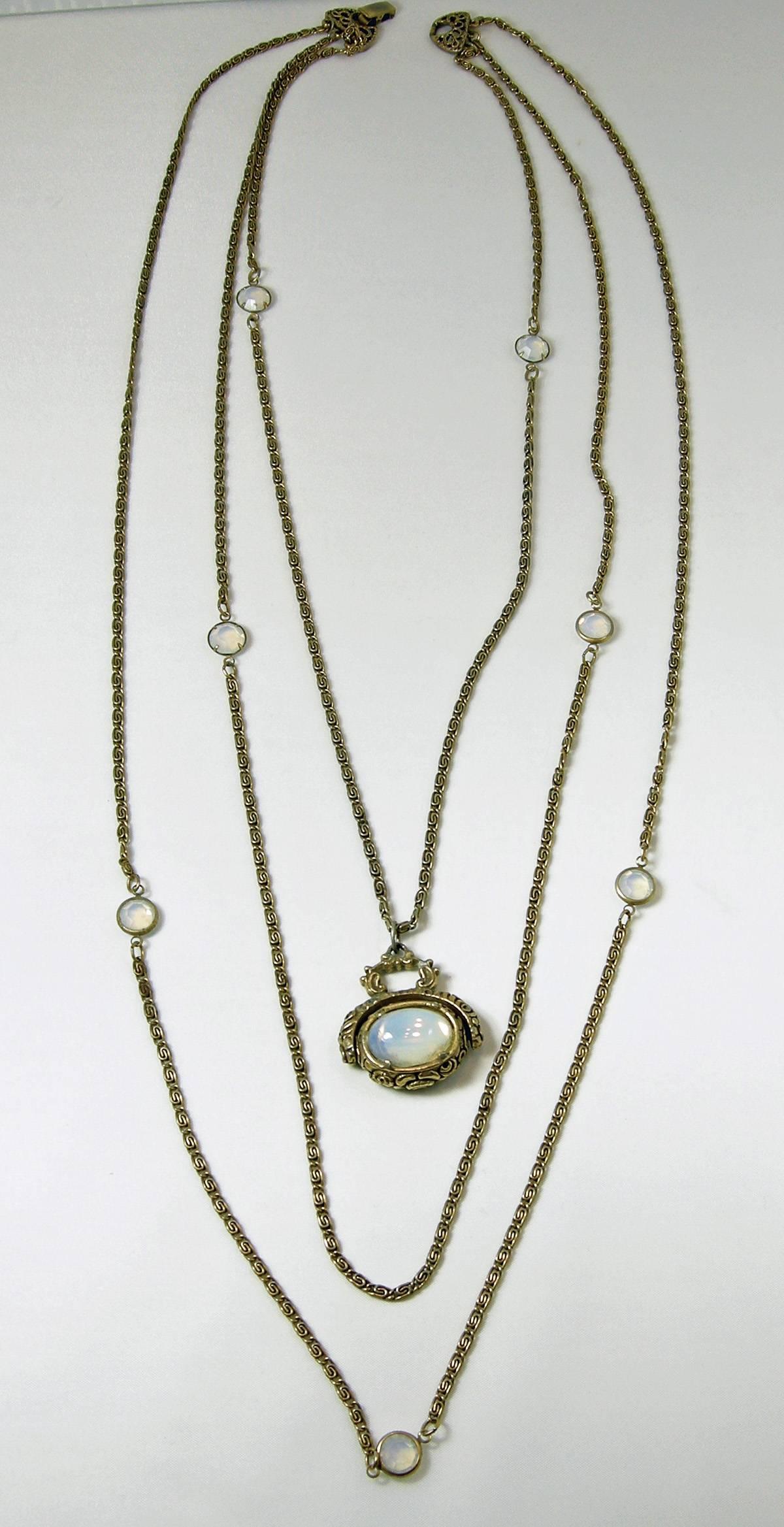 This stunning necklace is designed by Goldette that features a central spinner fob in opalescent glass. The longest chain measures 32, middle chain to longest measures 30”. The shortest measures 24”.  The fob is 1-1/2” x 1-1/4”.  It is in a gold