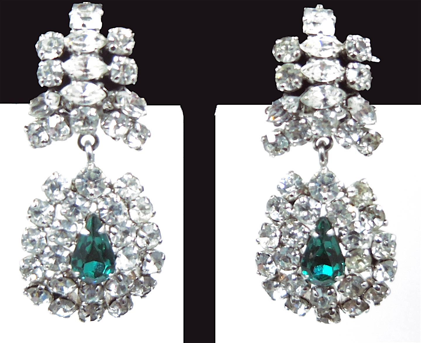 These gorgeous clip earrings are embellished with crystals on top and have an oval design at the drop with a faux green emerald in the center surrounded in layers with brilliant Austrian crystals. They are made in a silver tone setting and measure