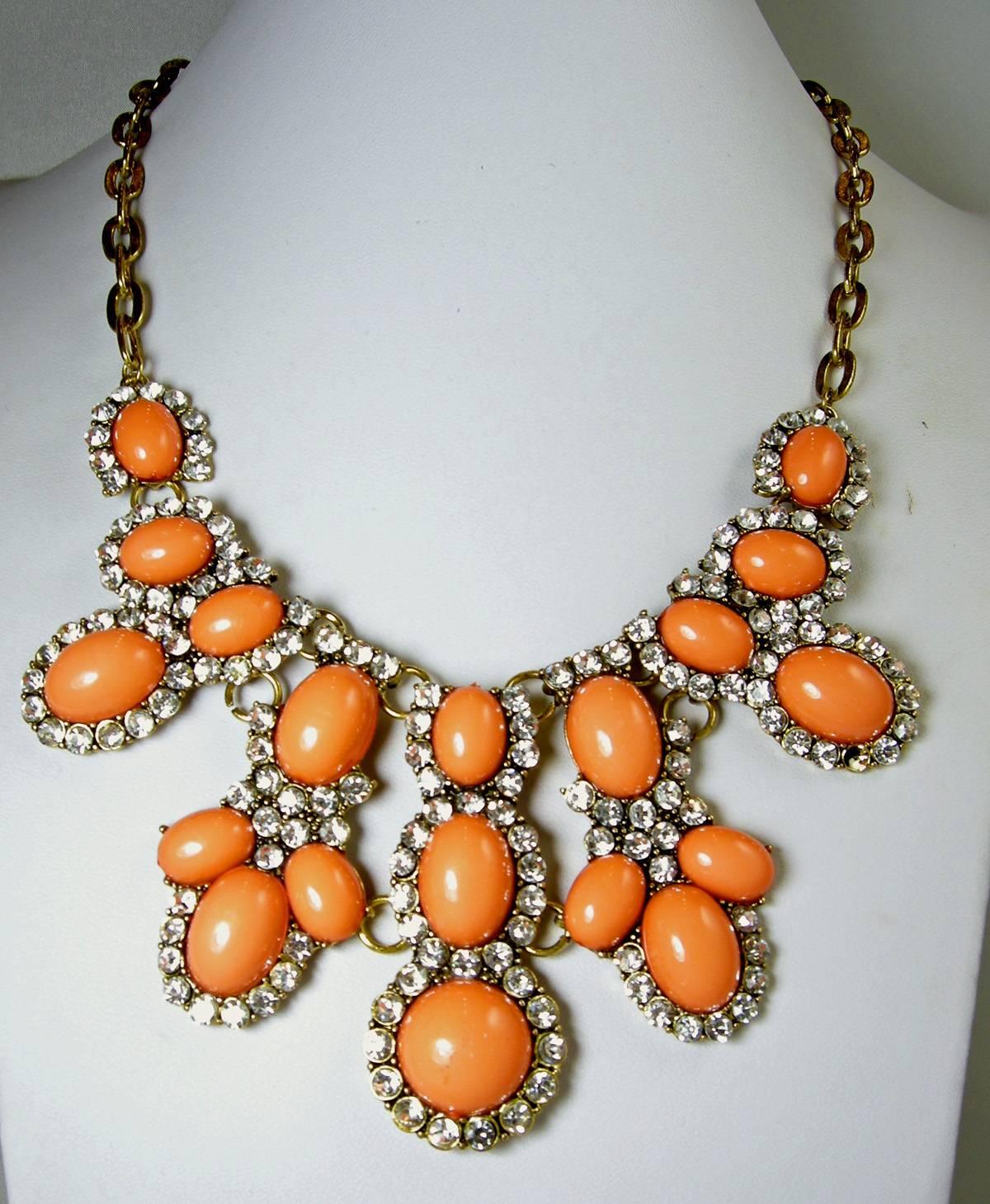 When I first saw this beautiful necklace I believed it was a Kenneth Jay Lane bib necklace. It features a centerpiece with faux coral colored cabochon stones all framed with rhinestones that came out in the late l960s. It has a brass tone open link