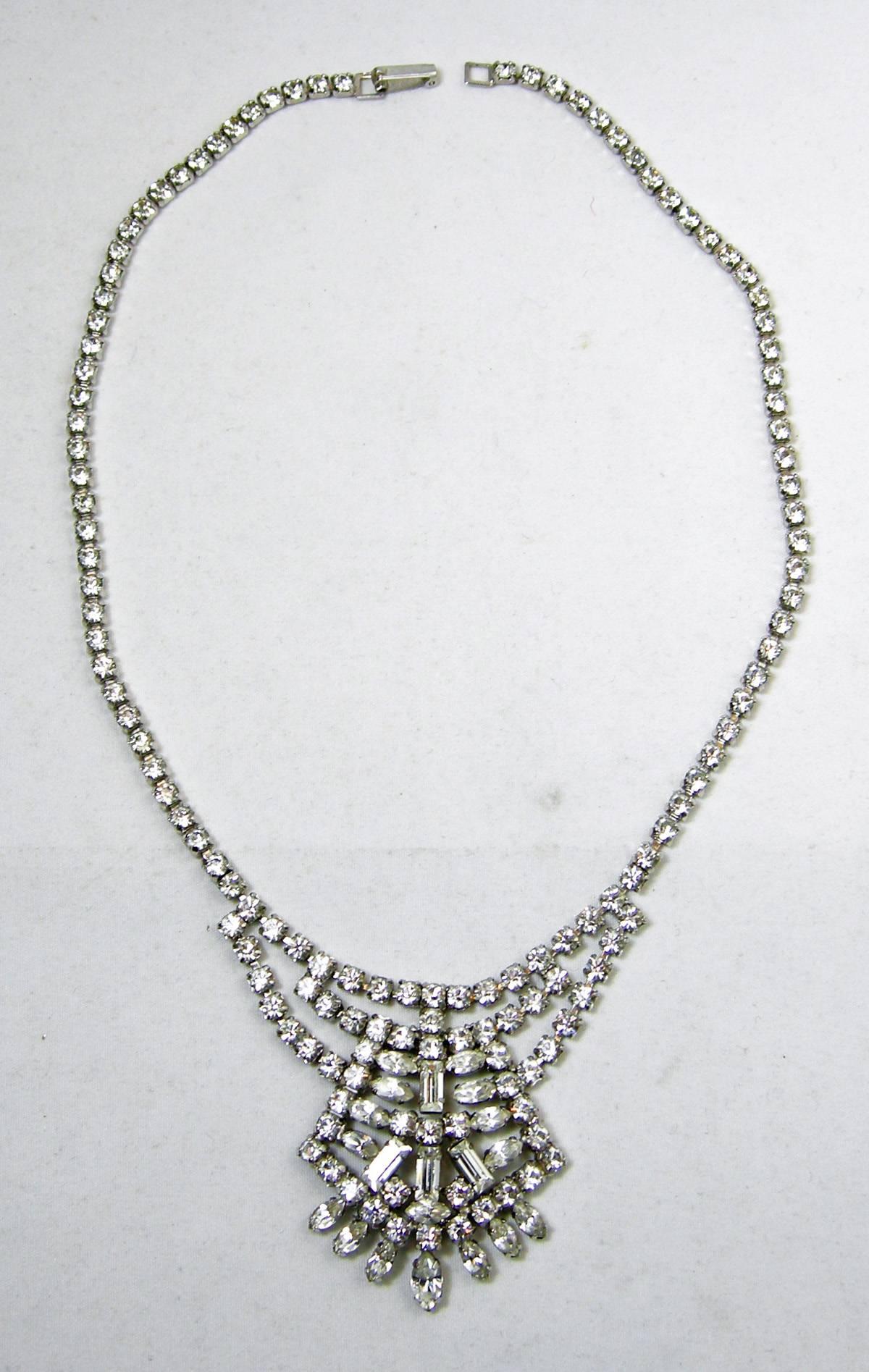 This stunning 1960s vintage necklace has a centerpiece that has a combination of teardrop, round and baguette shaped rhinestones. It is designed in a silver tone setting and measures 15”. The centerpiece measures 2” x 2-1/2”. It is in excellent