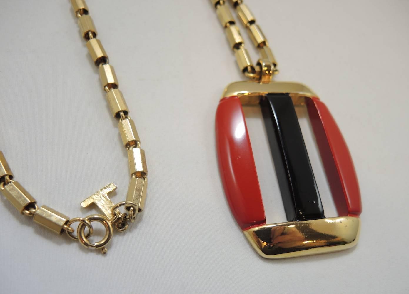 This is a classic Lanvin Of Paris large pendant necklace. It has a rectangular shaped pendant with an abstract design. There is red and black enamel with two openings in the center. It has the Lanvin’s famous link chain and is made in a gold tone