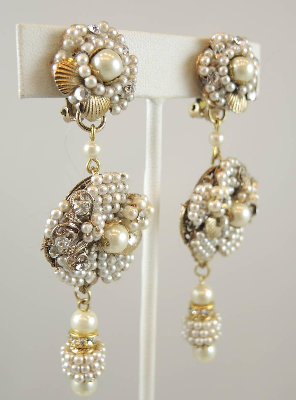 These are a fabulous pair of clip earrings designed by DeMario.  They feature a floral motif button top with faux seed pearls and a faux pearl center. There is a drop at the center with a large floral centerpiece of seed pearls and rhinestones. The