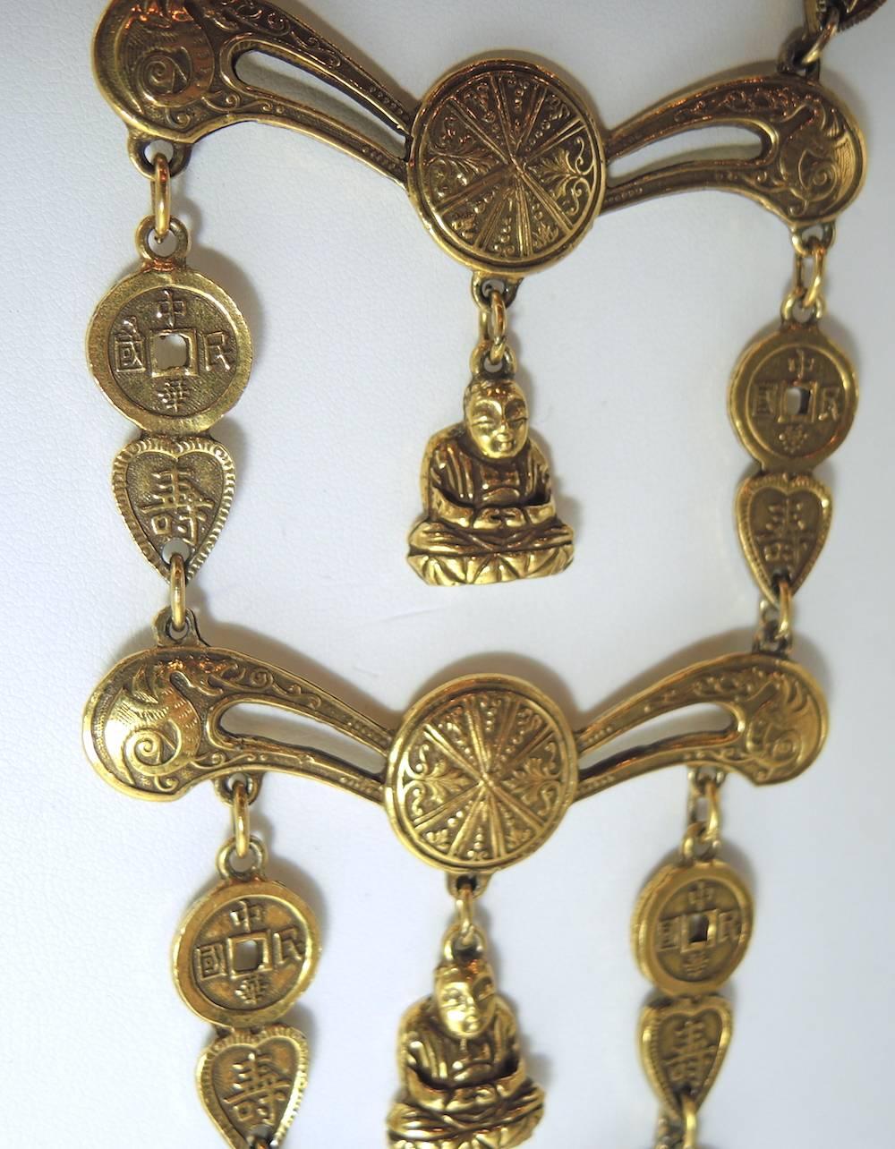 This 1950’s necklace was designed by Accessocraft and features a three-tiered necklace of round and heart shaped Asian symbols. All of the tiers have a Buddha in the center that dangles. This necklace is in a gold tone setting and measures 17” long.