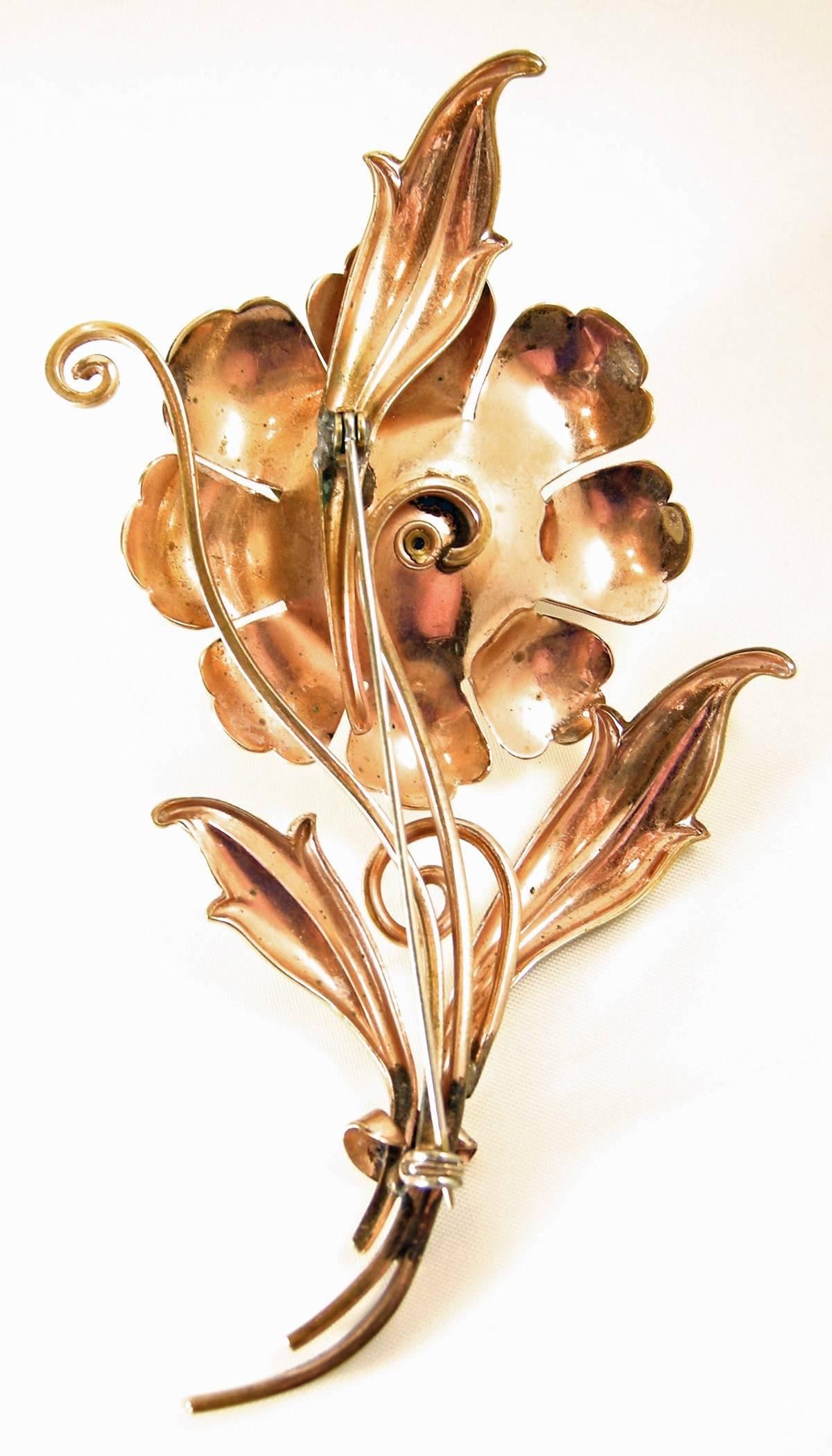 This is a huge flower brooch that is 5” long and 2-1/2” wide.  At first, I thought it sterling with a gold vermeil but there are no silver markings.  The brooch has leaves protruding at the bottom and at the very top from the flower.  The flower