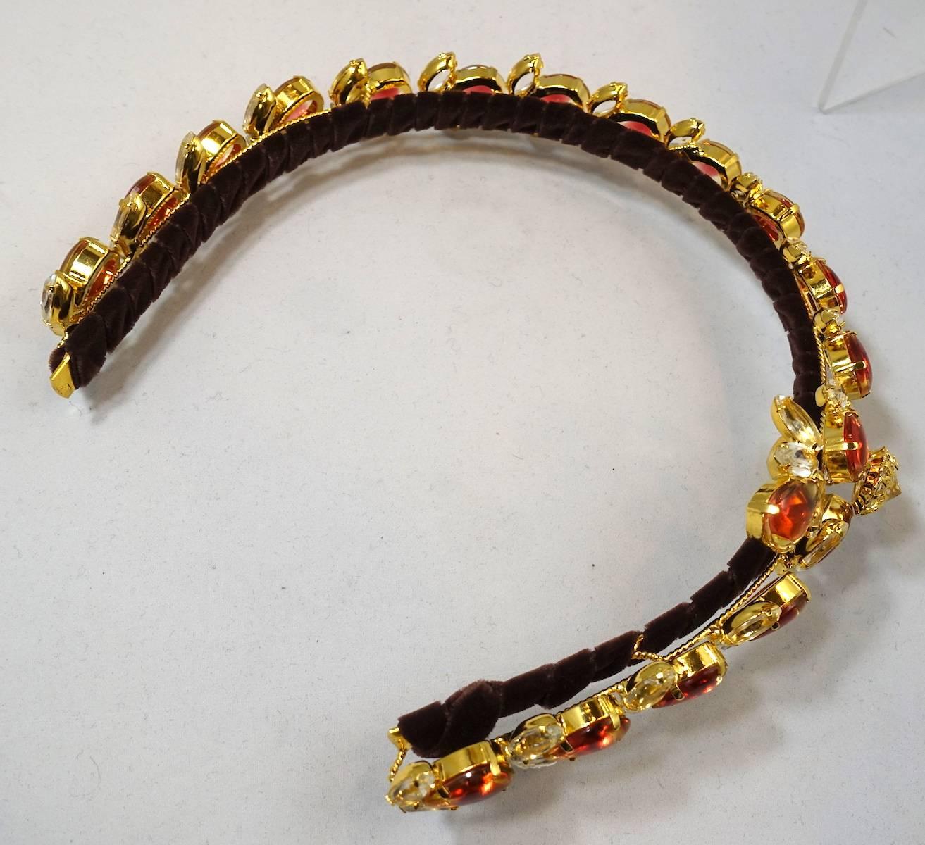 Robert Sorrell has done it again! He has created yet another headband that is unique. This one has orange and clear crystals in a floral design. The headband is in a rich gold tone setting wrapped around in brown velvet. It measures 17” x 1”. It is