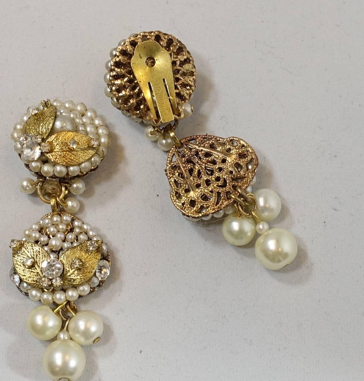 These 1950s faux pearl earrings were designed by Robert DeMario. They feature two round tops decorated with faux seed pearls, rose montee stones accented with golden leaves. It then has drops that continue with sead pearls and gold tone leaves.