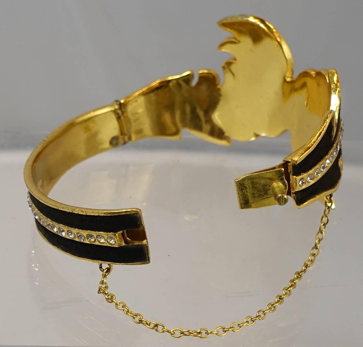 This vintage collectible book piece from the 1960s is a French bracelet with a feather design with black suede and brilliant rhinestones streaming throughout the center.  It is set in a gold tone metal finish. It has a slide in clasp with a safety