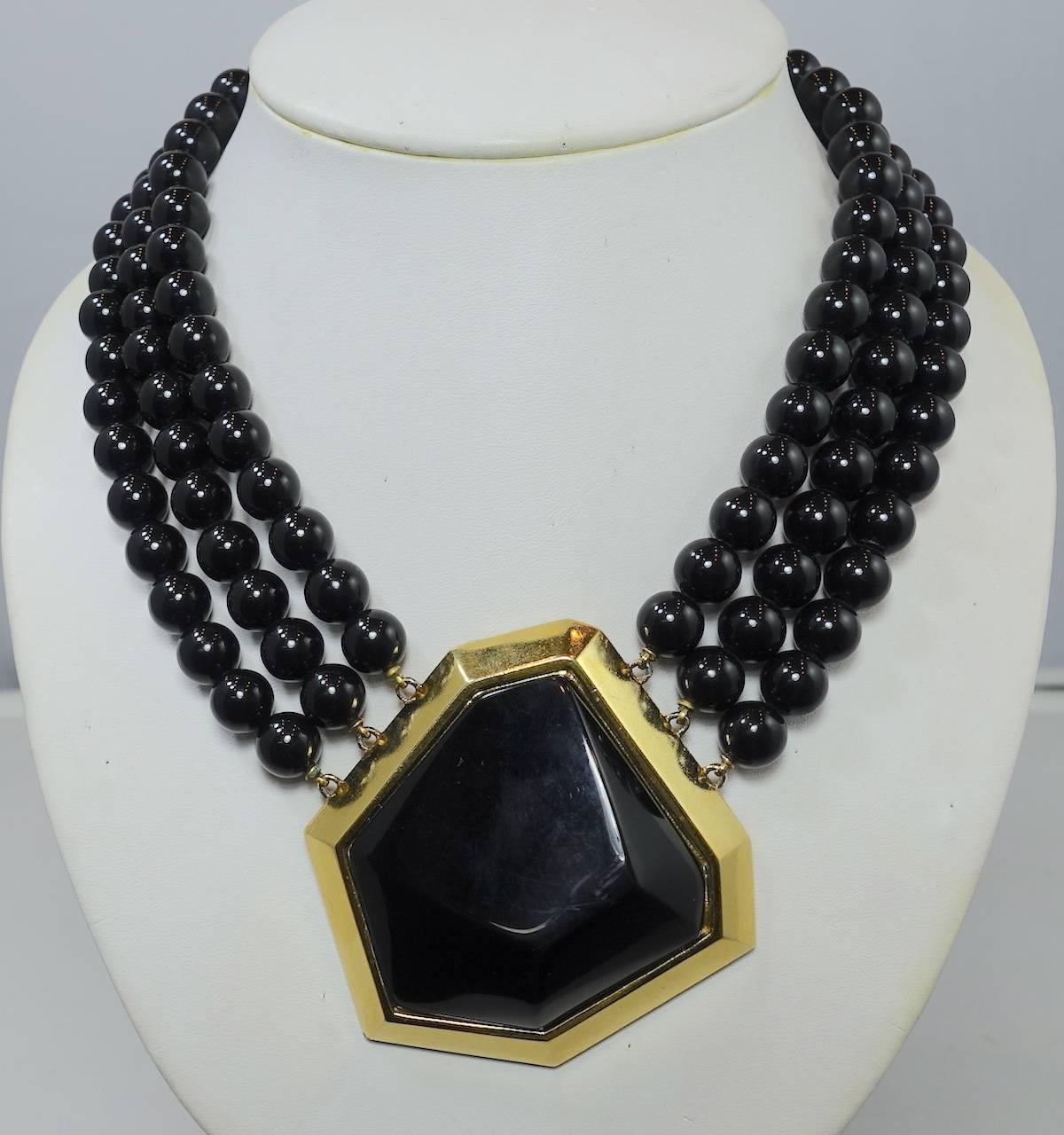 This great necklace was designed by Yves Saint Laurent.  Each side has 3 rows of glass black beads leading down to the modernistic shaped centerpiece. The centerpiece has a gold tone border embedded around a black modern shape. It has a hook clasp