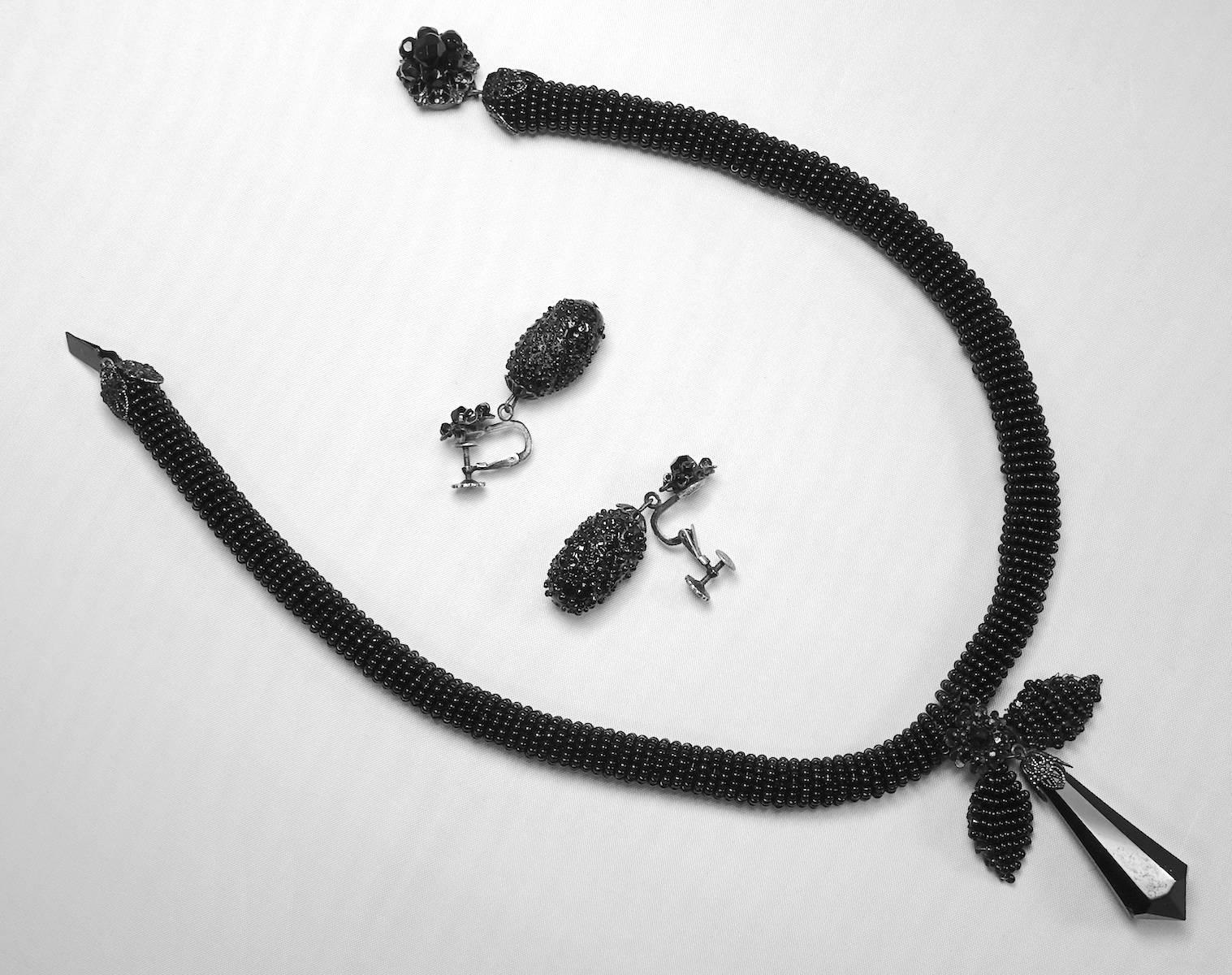 This rare vintage Miriam Haskell necklace and earrings set has tiny black jet seed beads in a japanned setting. The necklace measures 16” x 1/2” with a slide in clasp.  The matching screw-back earrings are 1-1/2” x 1/2”. This set is signed “Miriam