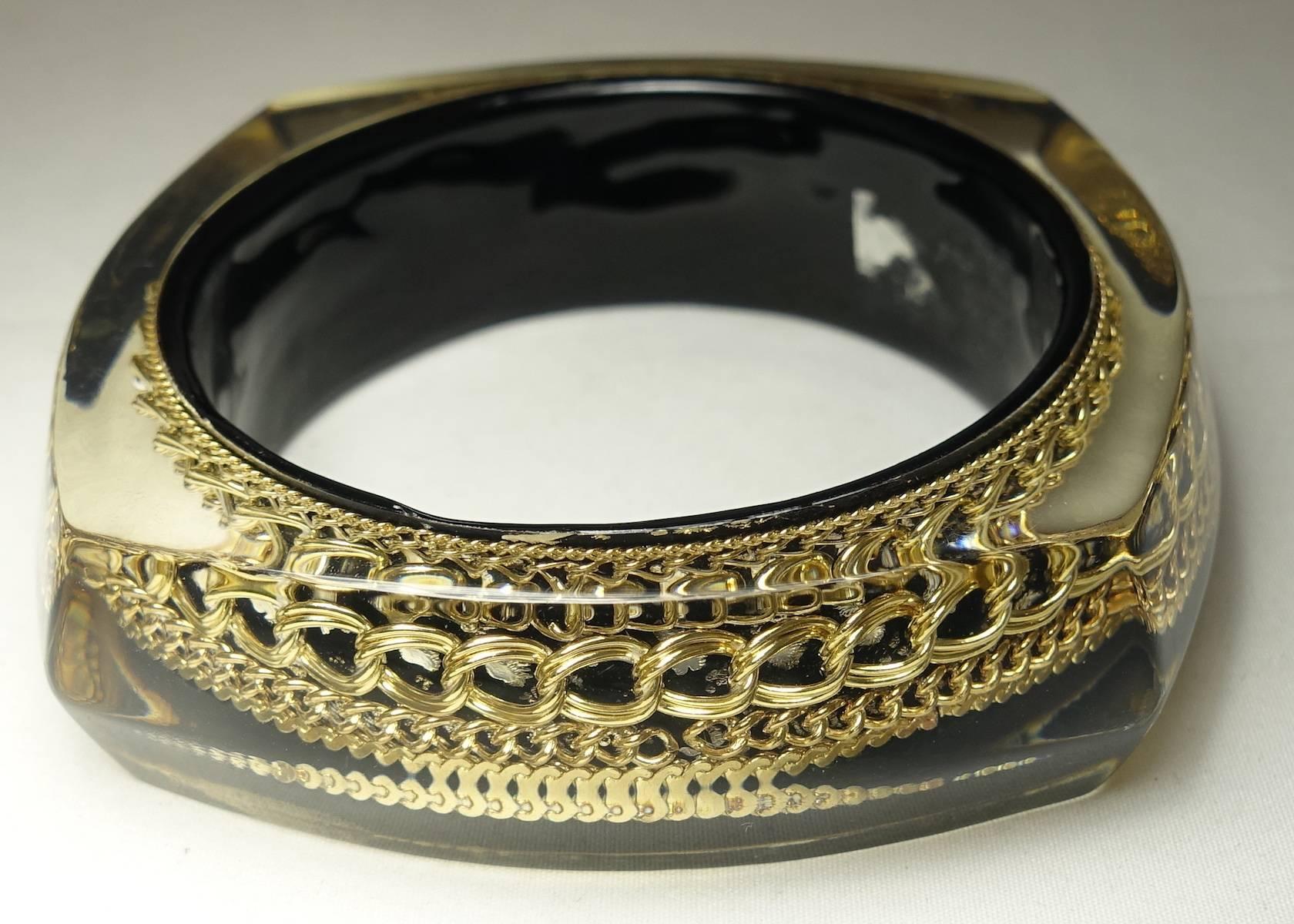 This vintage Lucite bangle bracelet has multiple gold tone link chains embedded within. It has a curved-edge, square-shape and measures 3-1/4” wide x 1” and can fit up to an 8” wrist.  This bangle is in excellent condition.