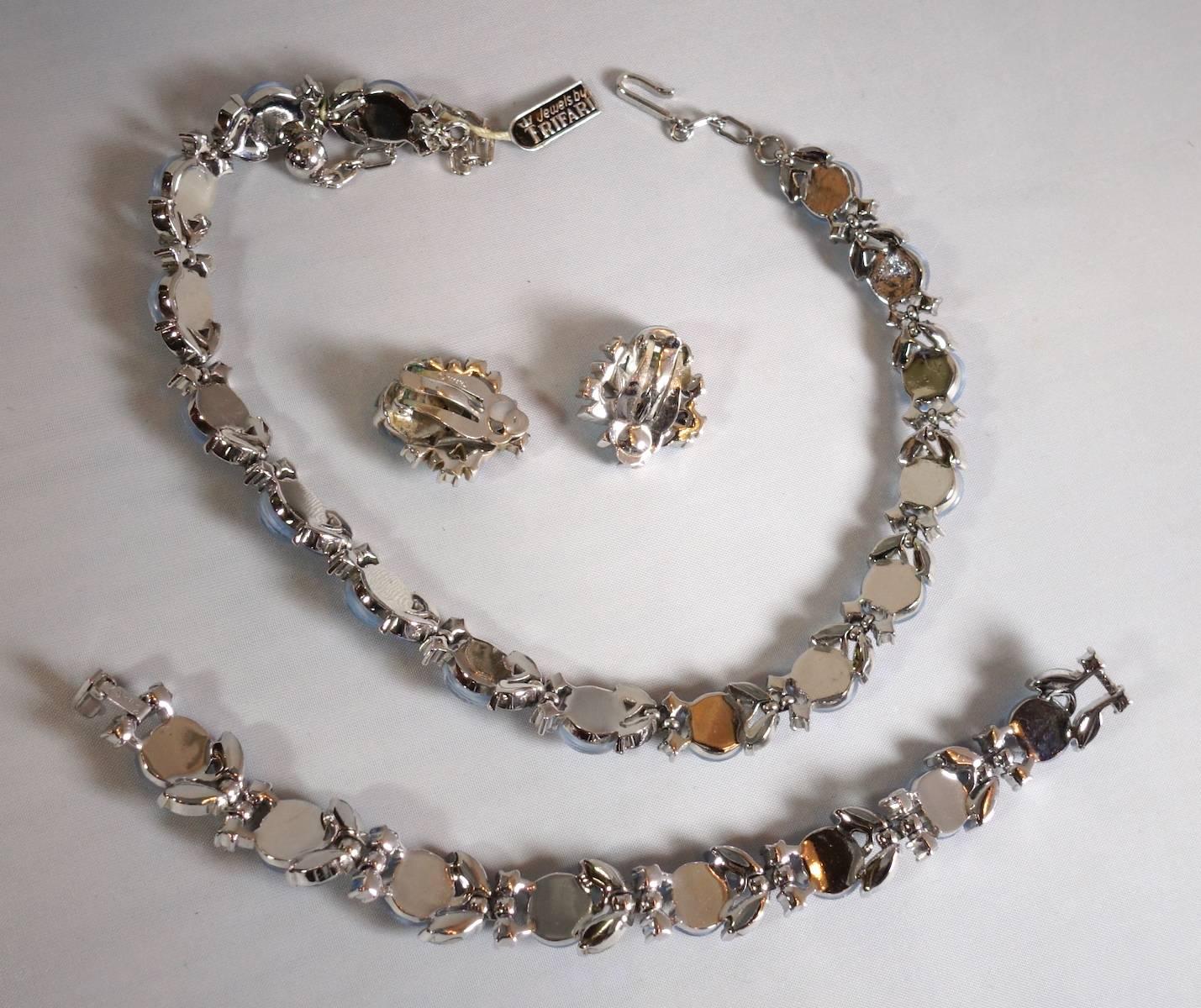 This famous vintage 1930s Trifari set features hues of blue glass moonstone buttons with clear and red crystal accents in a rhodium silver tone setting. The necklace measures 16” x 1/2”.  The matching bracelet is 6-1/2” x 1/2” and matching the clip