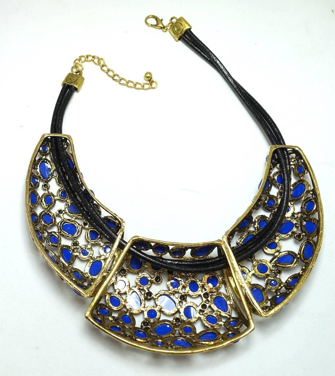 This unsigned Oscar de la Renta necklace features three sections with cobalt blue cabochon stones in a gold-tone setting. It is connected on a double row of leather straps with spring closure. The necklace measures 18” x 3-1/2” at the widest point