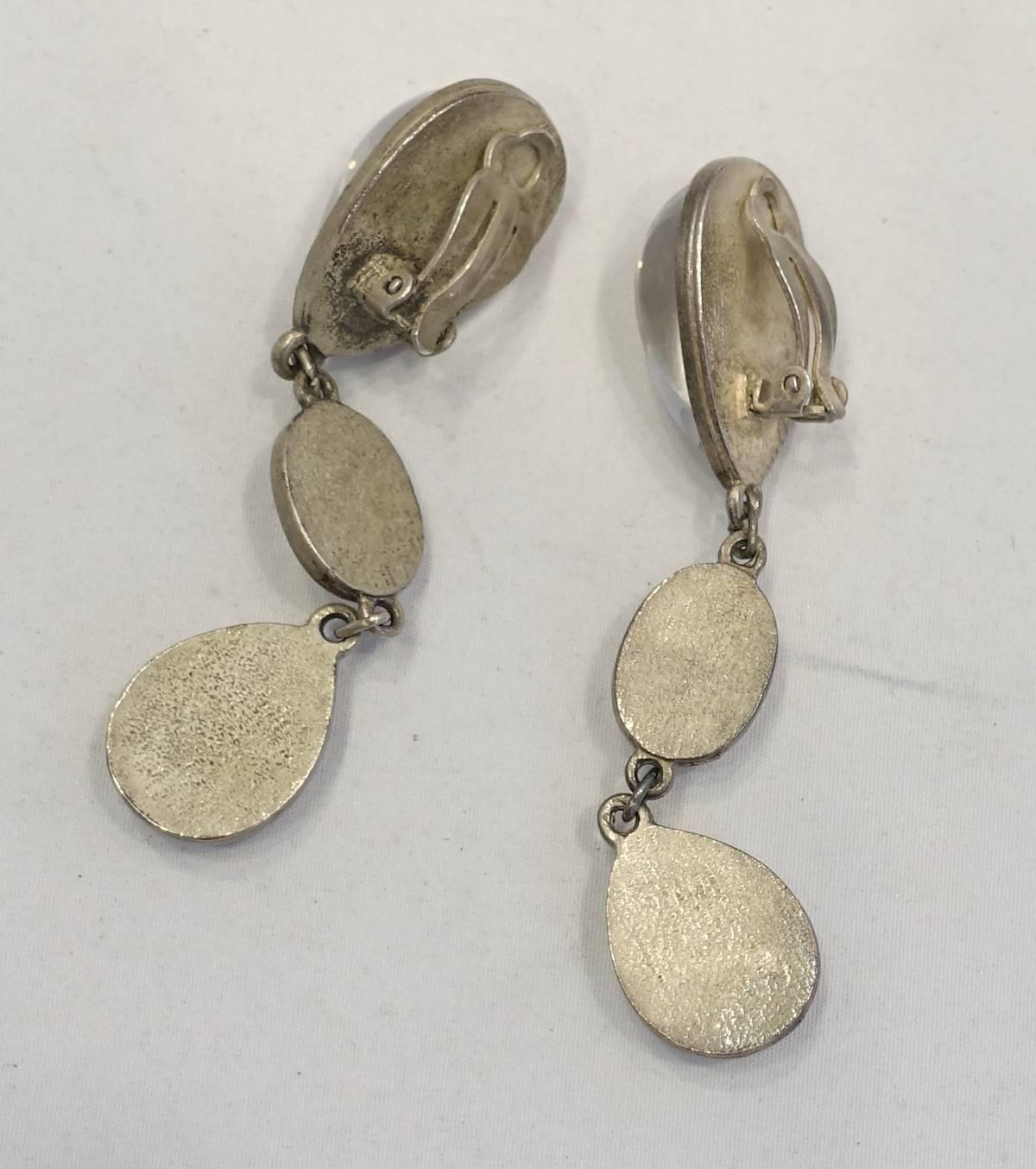 These statement earrings each feature clear cabochon stones in a silver tone setting.  These clip earrings measure 3-1/4” x 3/4” and are in excellent condition.