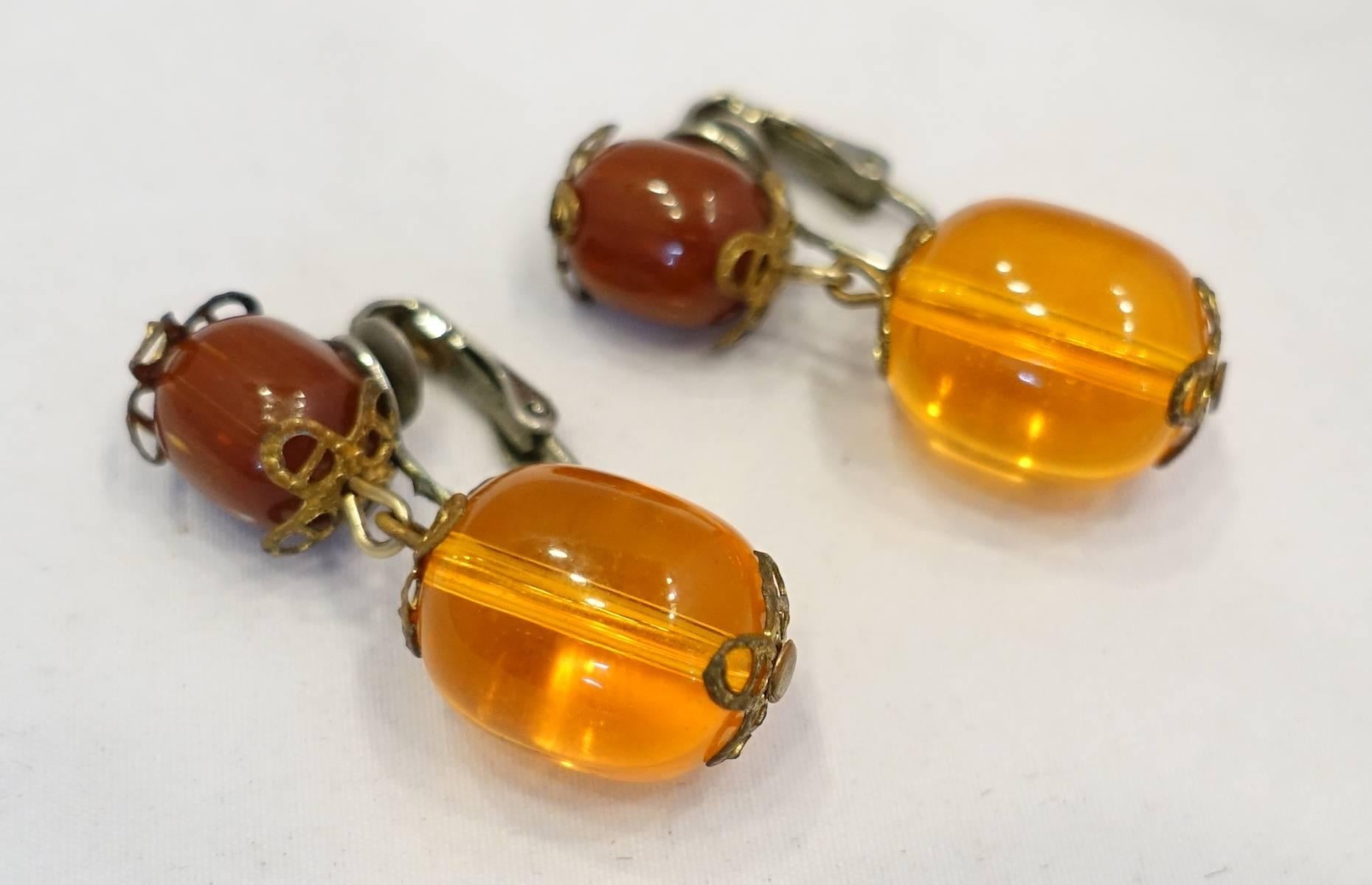 These vintage 1960s earrings feature a red bead top with a faux amber drop in a silver tone setting. These clip earrings measure 1-1/2” x 1/4” and are in excellent condition.