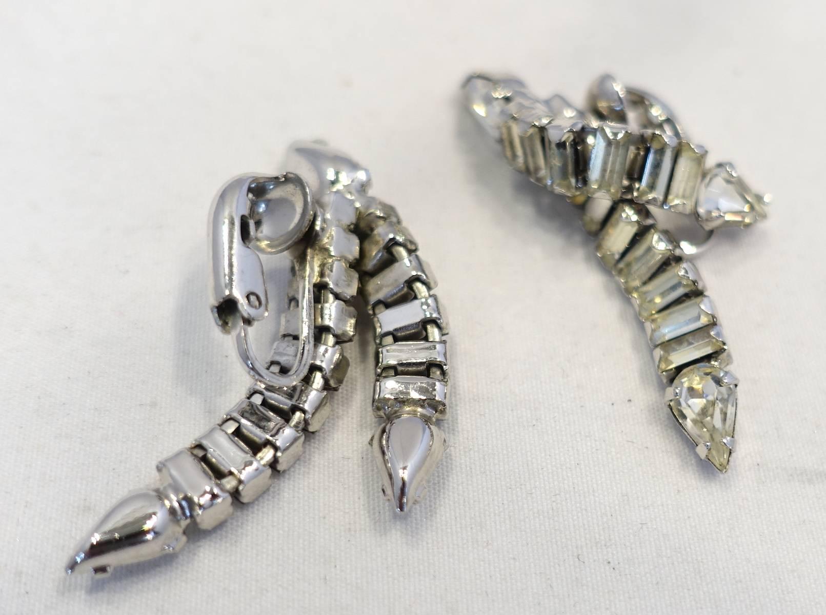 These vintage 1950s drop earrings feature two rows of clear crystals falling downward. They are in a silver tone setting.  These clip earrings measure 1-3/4” x 1/2” and are in excellent condition.