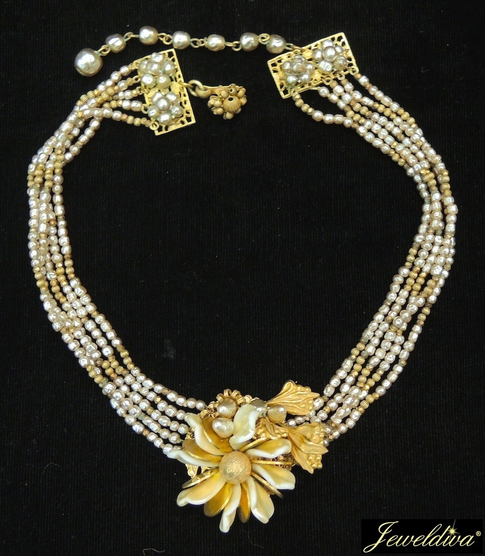 This vintage signed Miriam Haskell necklace features a floral centerpiece with MOP petals and faux pearls in a gold-tone setting.  The centerpiece measures 1 7/8” x 1 ½”; the necklace is 17” long with a hook closure.  This vintage necklace is signed