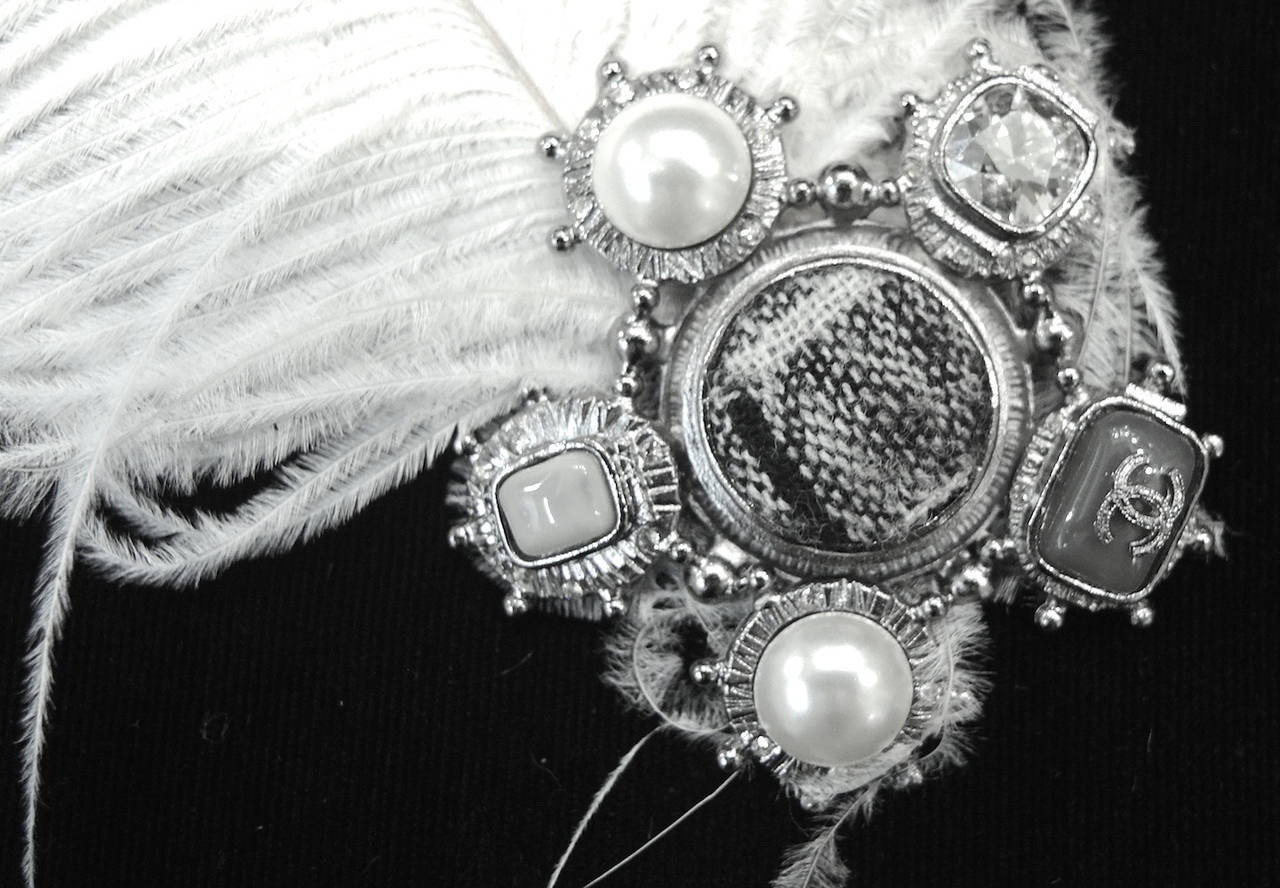 This suddenly famous Chanel pin features a white feather attached to a Chanel pin with clear rhinestones, faux pearls and the CC logo.  This pin alone is 2 ½” in diameter and has a turn closure; with the attached feather, it is 9 ½” long x 7” wide. 