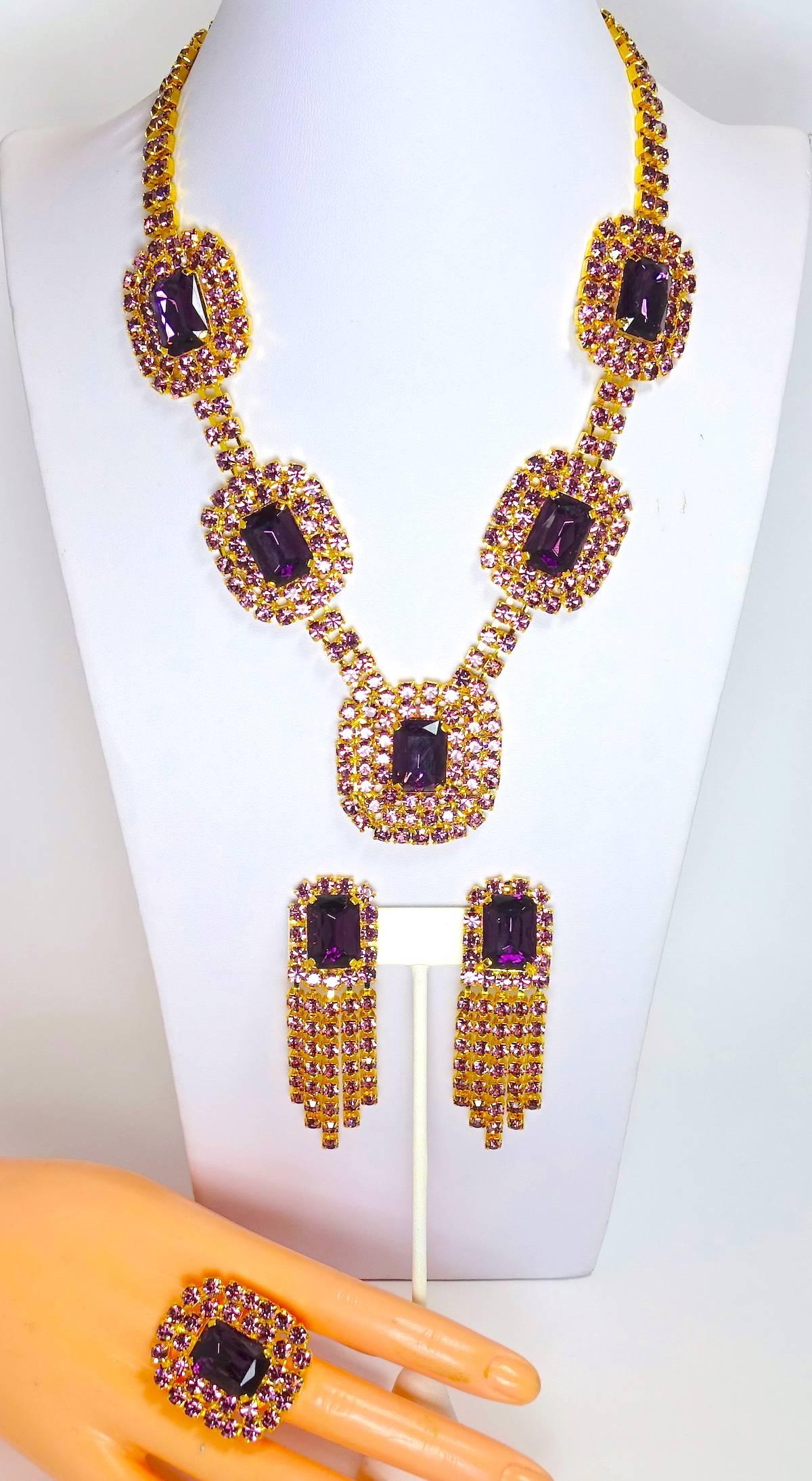This stunning Czech set features light and dark amethyst color crystals in a gold tone setting.  The necklace measures 21” long x 1-1/8”; the front drop is 1-5/8” x 1-1/2”.  The dangling clip earrings are 2-3/4” x 7/8”. The ring is adjustable up to
