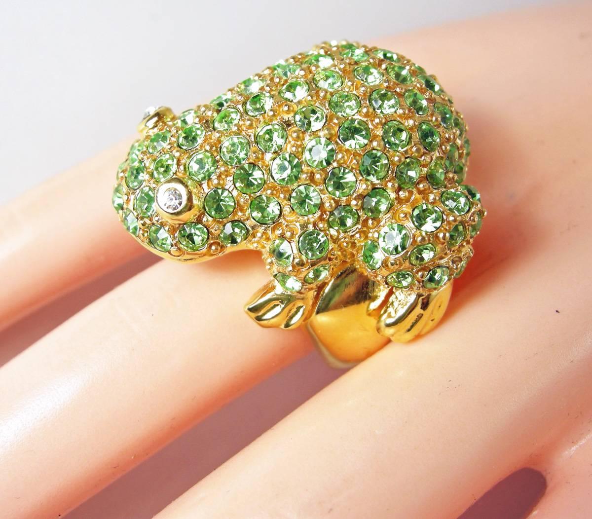 This is a wonderful ring by Kenneth Jay Lane.  It is a green frog embedded with bright green rhinestones.  It is a gold tone setting.  The ring size is 7-3/4 with a ring guard inside.  It is signed “Kenneth Lane” and in excellent condition.