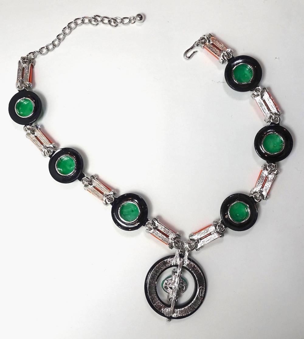 This signed Kenneth Jay Lane necklace features an Asian theme design with carved faux jade, coral, onyx with crystal accents in a silver-plated base metal setting.  This necklace measures 20” long with a hook closure; the front drop is 1-1/2”