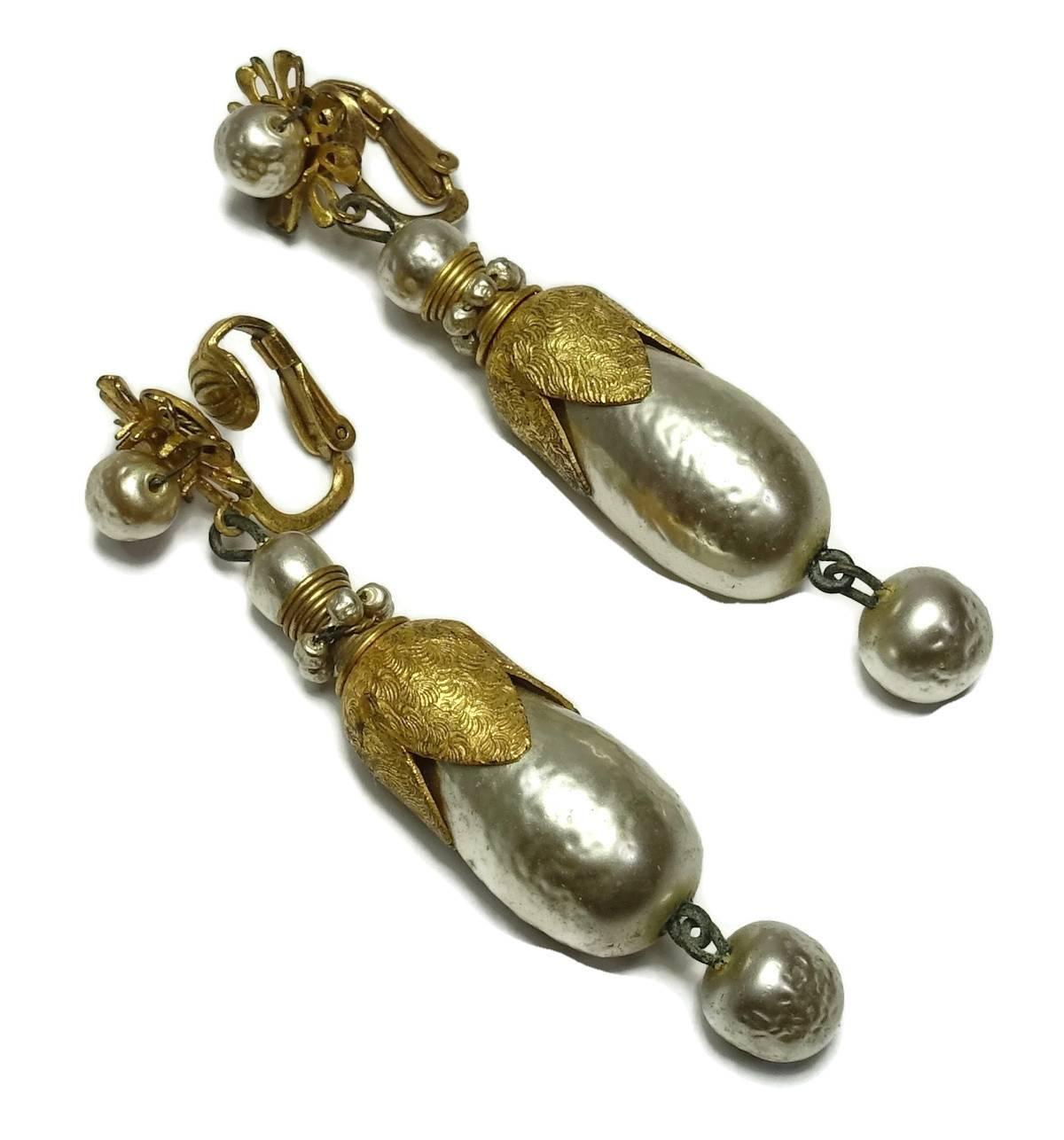 These vintage 1950s signed Miriam Haskell earrings are rare.  The top has a floral design with a faux pearl center that leads down to a long faux pearl center that has a gold plate cap. At the bottom hangs another faux pearl. It is made with a