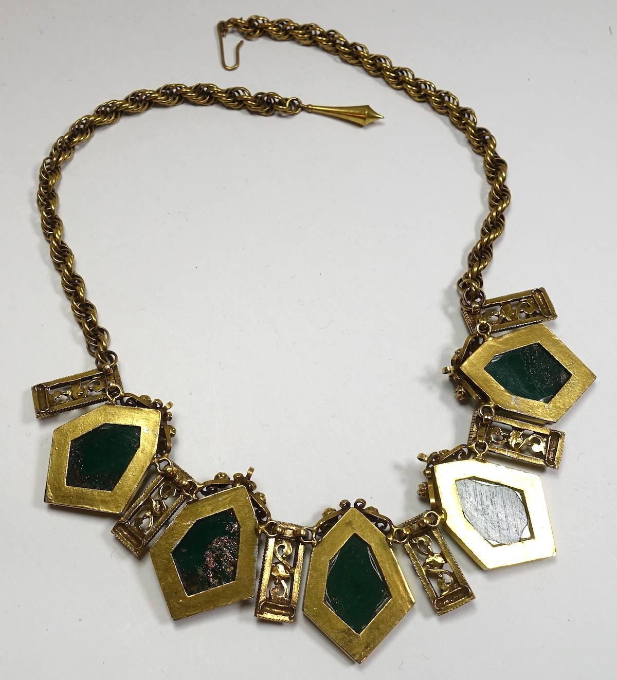 This vintage 1940s necklace features faux coral and green foiled stones in a gold-plated base metal setting.  This necklace measures 20” x 1-3/4” with a hook closure and is in excellent condition.