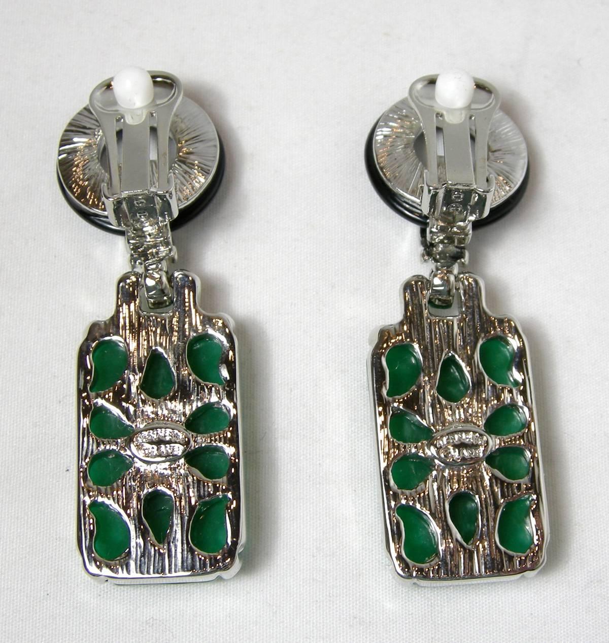 These signed Kenneth Lane earrings feature a carved floral design in faux jade with onyx enameling and clear crystal accents in a silver-plated base metal setting.  These clip earrings measure 2” x ¾”, are signed “Kenneth Lane” and are in excellent