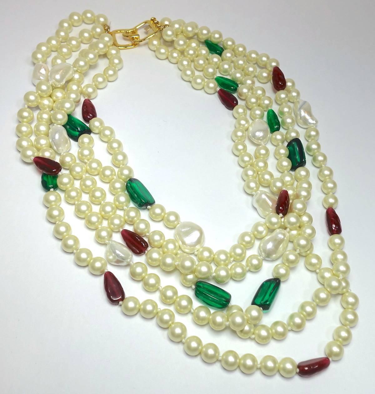 This signed Kenneth Lane necklace features 5 strands of faux pearls with green & red stone accents in a nickel-free gold-plated base metal setting.  The necklace measures 17-1/2” with each row graduating in length.  It has hook closure and the