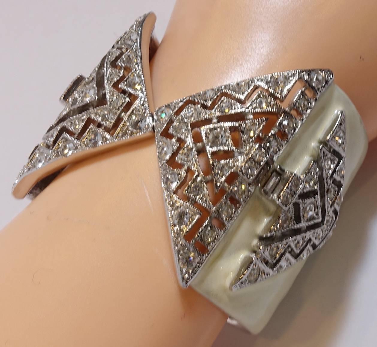 This signed Kenneth Jay Lane bracelet features clear crystals on an ivory color enameling on a nickel-free silver-plated base metal setting.  This bracelet measures 6-3/4” around the inside x 2” wide and is signed “KJL”.  It is in excellent