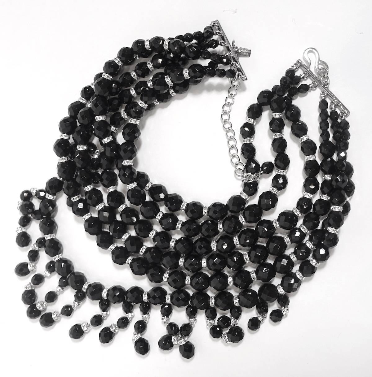 This signed Kenneth Lane beaded bib necklace features 6 strands of faceted black glass beads with rhondelle crystal spacers in a nickel-free silver-plated base metal setting.  This necklace measures 18” long with a hook closure.  The center falls