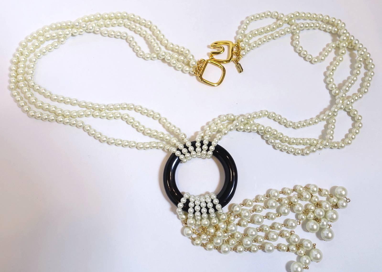 This signed Kenneth Lane necklace features faux pearls encircling a black enameled hoop in a nickel-free gold-plated base metal setting.  This necklace measures 30” long with a hook closure. The pearls on the neckpiece are 1/4” wide.  The center