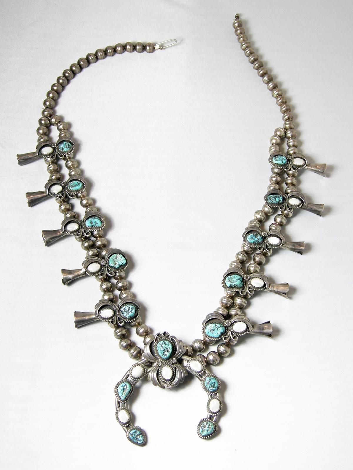 This magnificent necklace is sterling silver with silver beads leading down to a double row of silver beads.  You have 5 segments on each side with turquoise and mother of pearl with horn like ends.  All the stones are bezel with an ornate silver