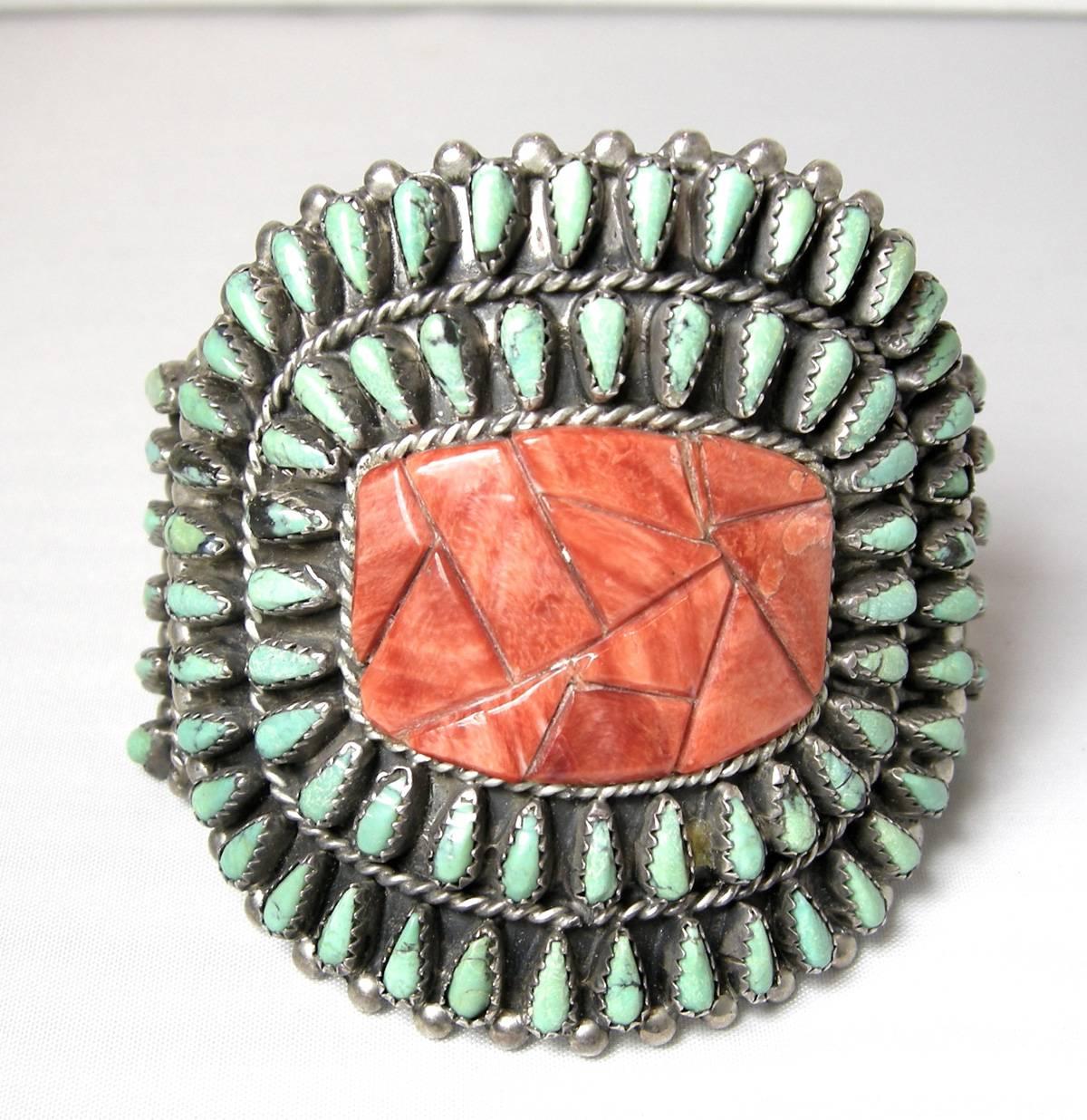 This sterling Zuni turquoise cuff has a needlepoint design on the outside with a carved coral center.  All the turquoise stones are bezel set with sterling rims.  It measures 2-1/2” x 2-1/2