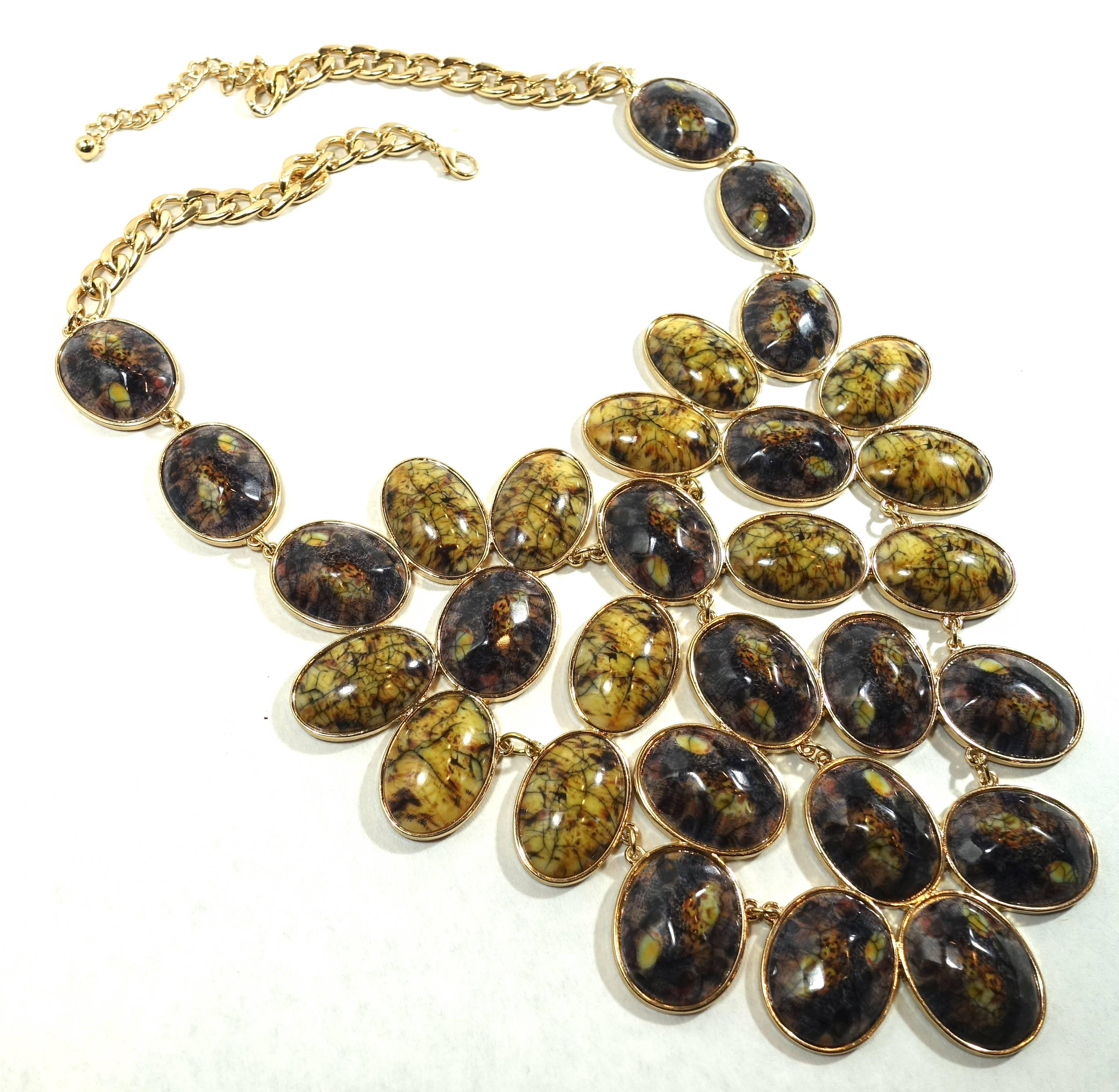 This huge bib necklace features different shades of Dichotic stones in a gold tone setting. It has link chain and is wide at the top and lessens to the bottom. The necklace measures 24” with a spring closure. The front, top to bottom, is 6-1/2”. 
